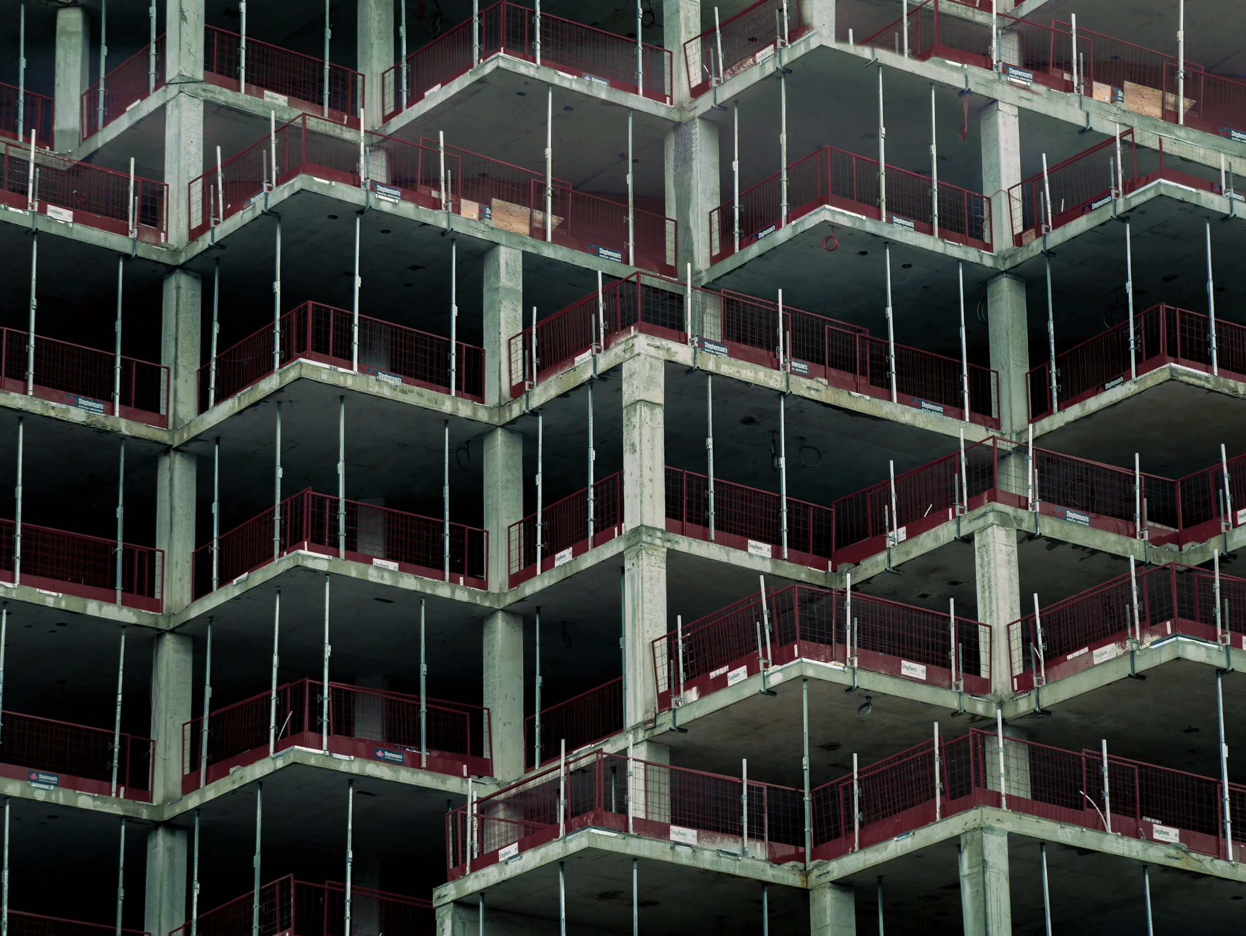 Multiple floors of a building under construction with concrete and red safety railings.