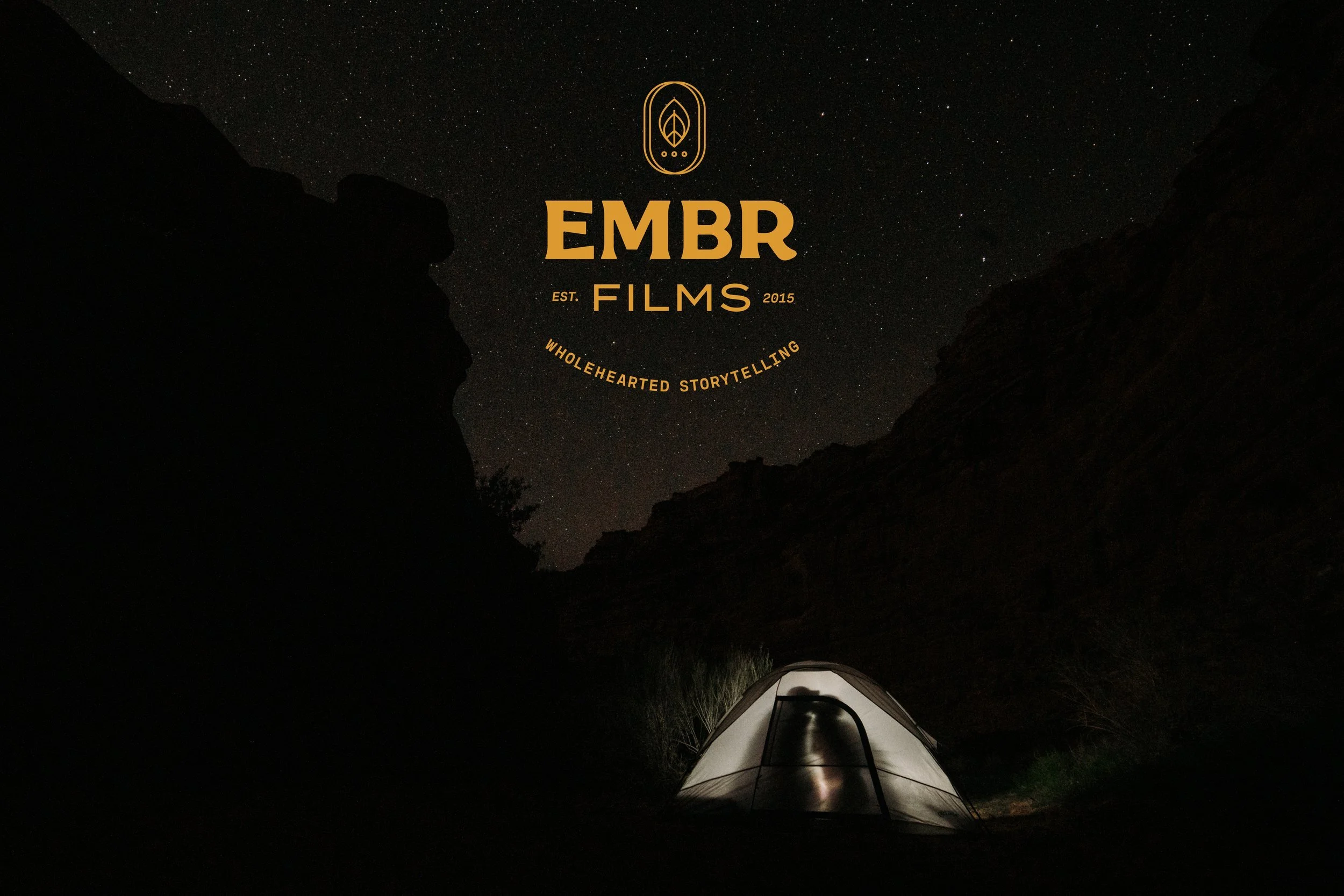 A tent illuminated from inside, set up in a dark canyon at night with a starry sky overhead.