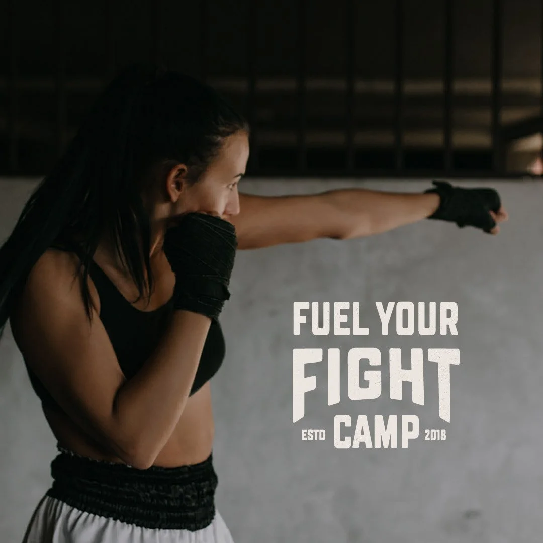 A woman boxing at a gym, wearing black gloves, a black sports bra, and white shorts, with her left arm extended in a punch, and text in the image reads 'Fuel Your Fight Camp Estd 2018'.