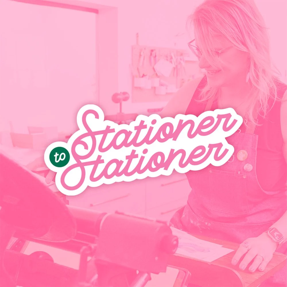 A woman with blonde hair wearing glasses and a pink apron, smiling in a creative workspace with craft supplies in the background, overlaid with the text "to Stationer to Stationer."