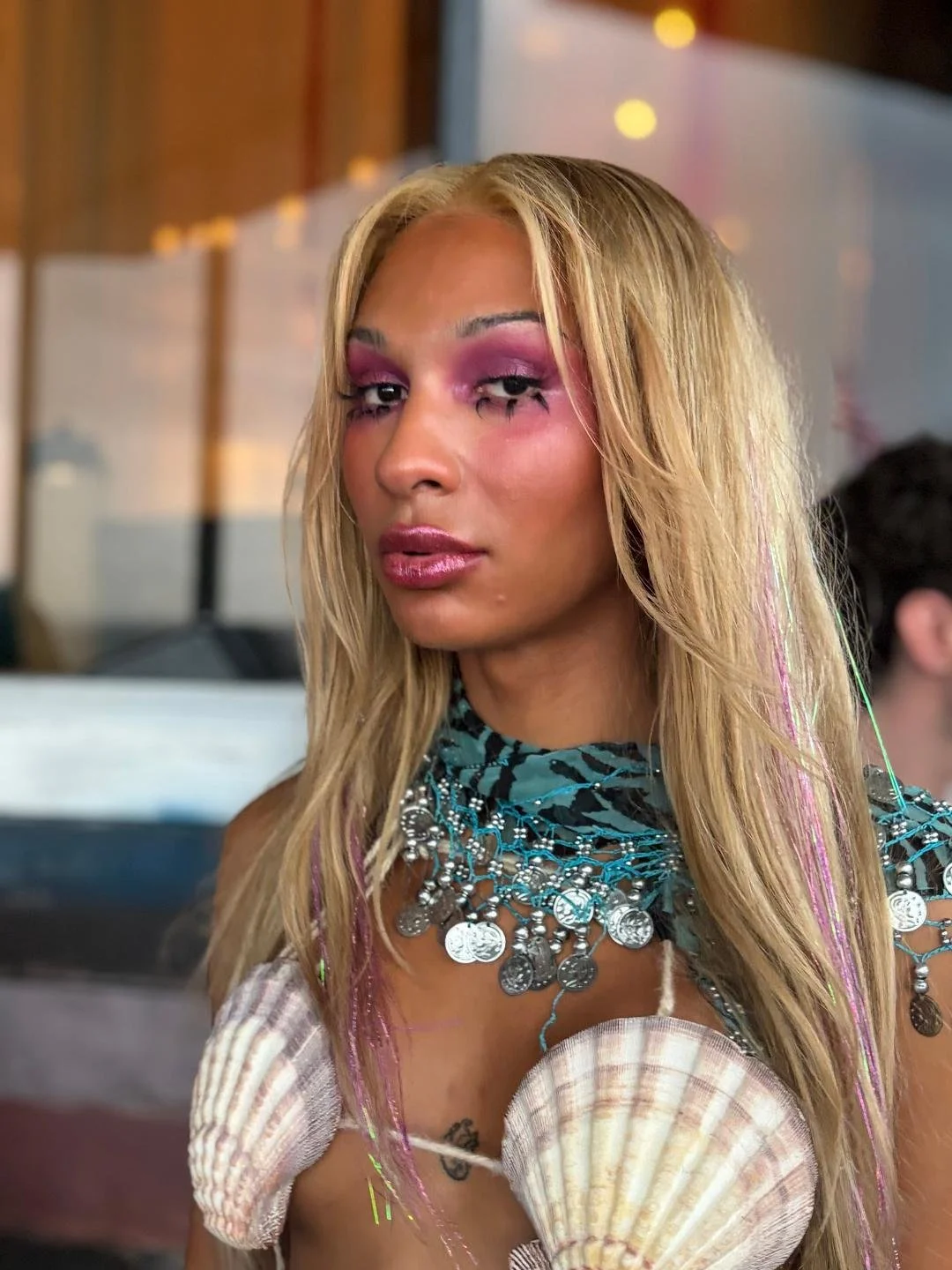 A woman in a shell bikini and shawl with spiky lashes and burgandy eyeshadow and glossy lips