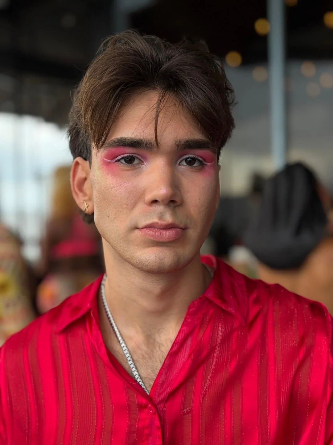 A man in a red shirt with pink eyeshadow and makeup