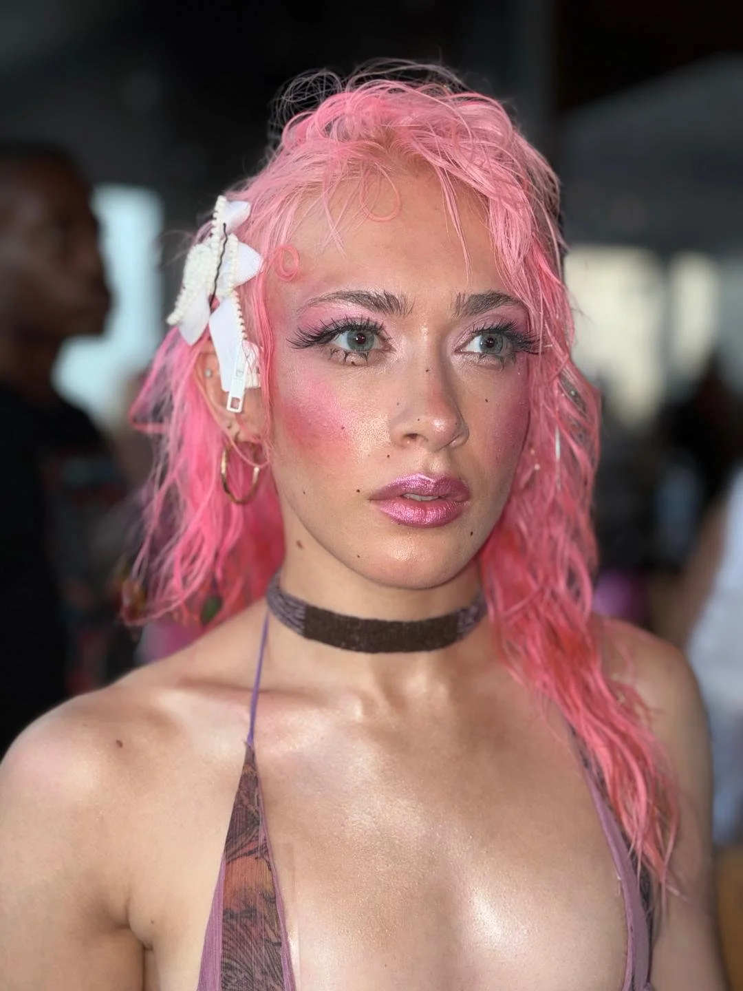 A woman with pink hair and bright blush and glitter makeup wearing a bikini