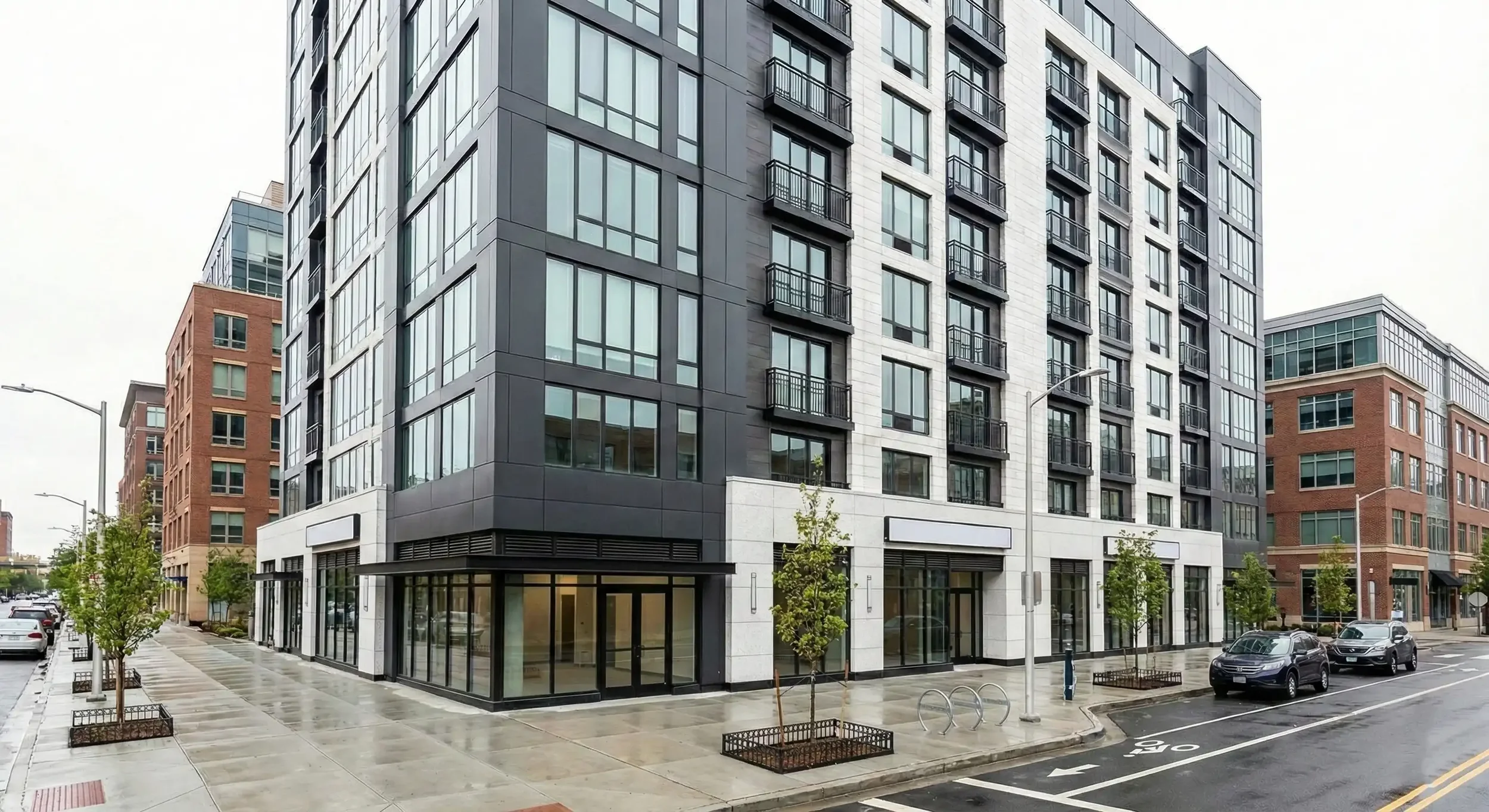 Modern multi-story apartment building with glass windows, storefronts, and balconies, located on a city street with parked cars, small trees, and magazine stands. Ravenswood Chicago multifamily property