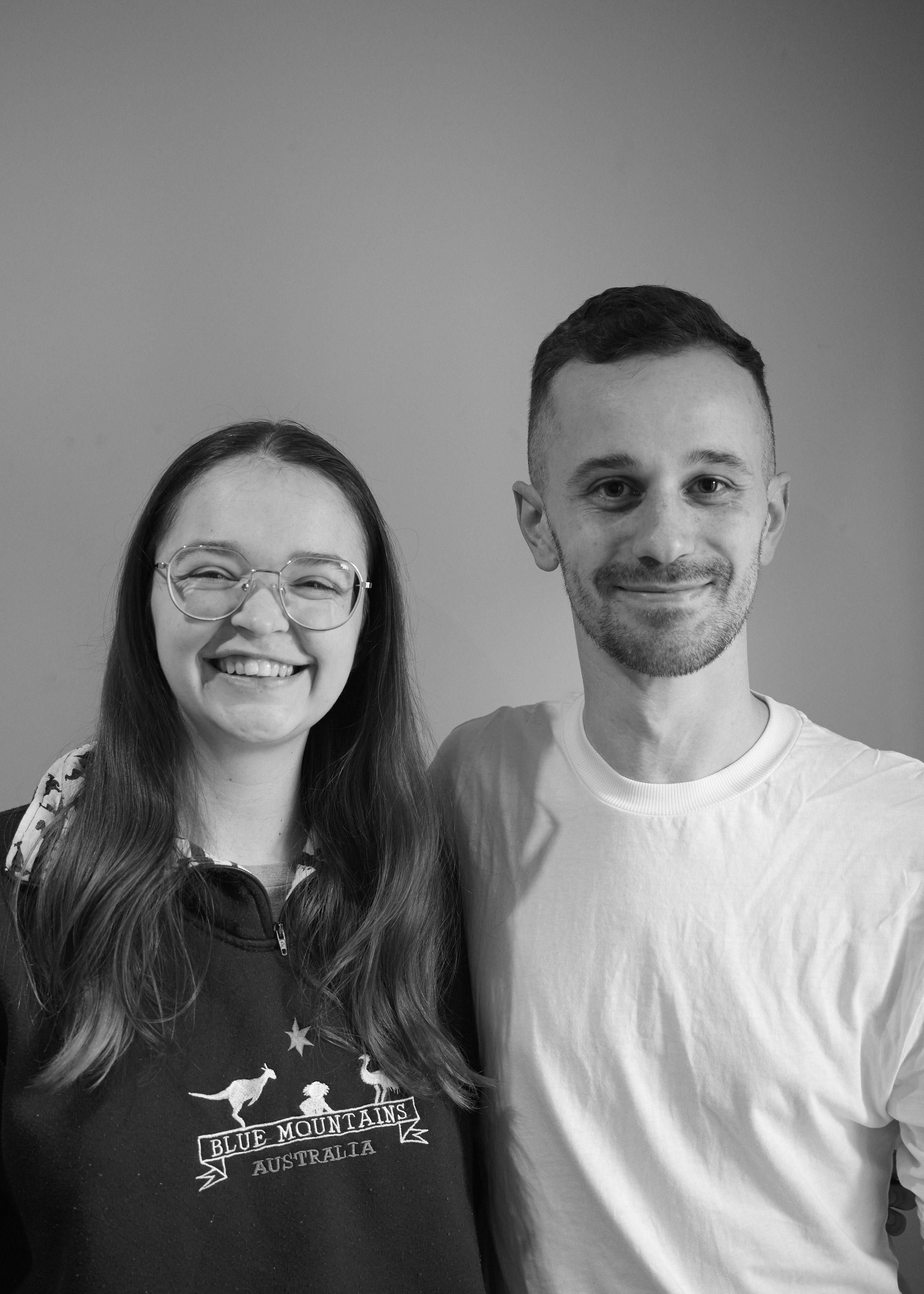 Two people, one man and one woman, smile at a camera. The photo is in black and white and they look cheerful