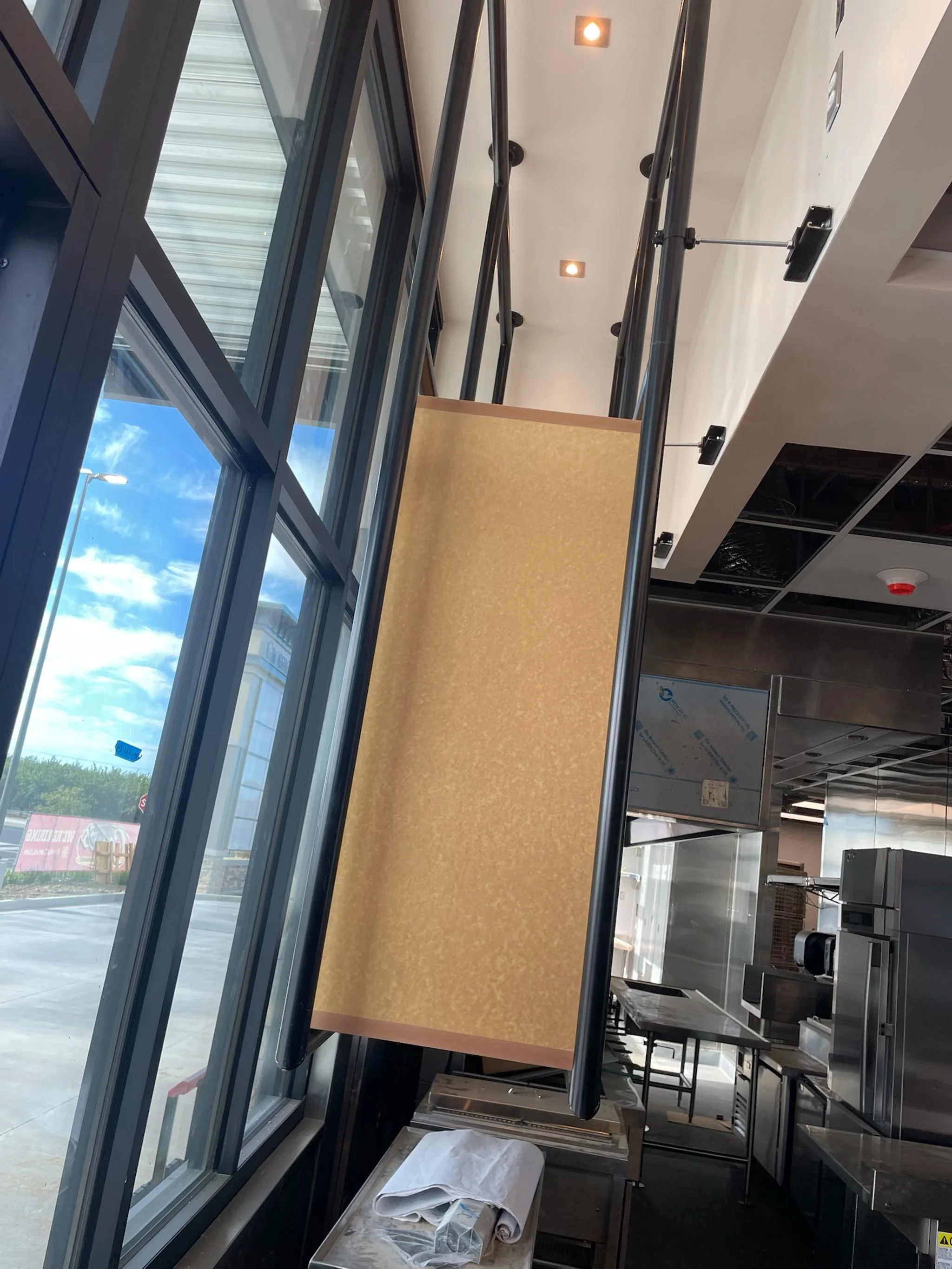 Empty restaurant or cafeteria with a large window, a counter with a beige partition, and industrial kitchen equipment in the background.