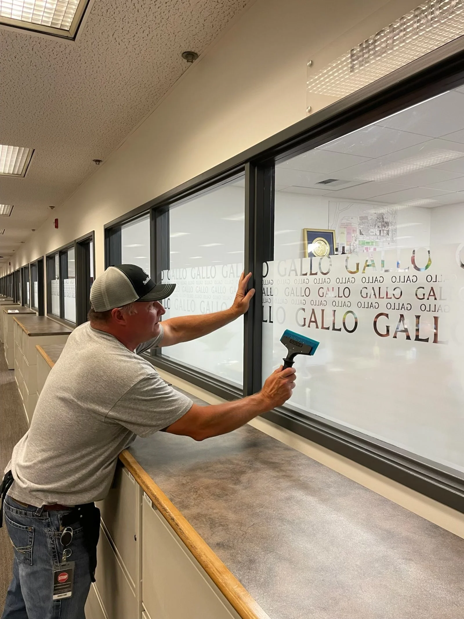 A man applying colored vinyl lettering to a glass window, spelling out the word "GALO."