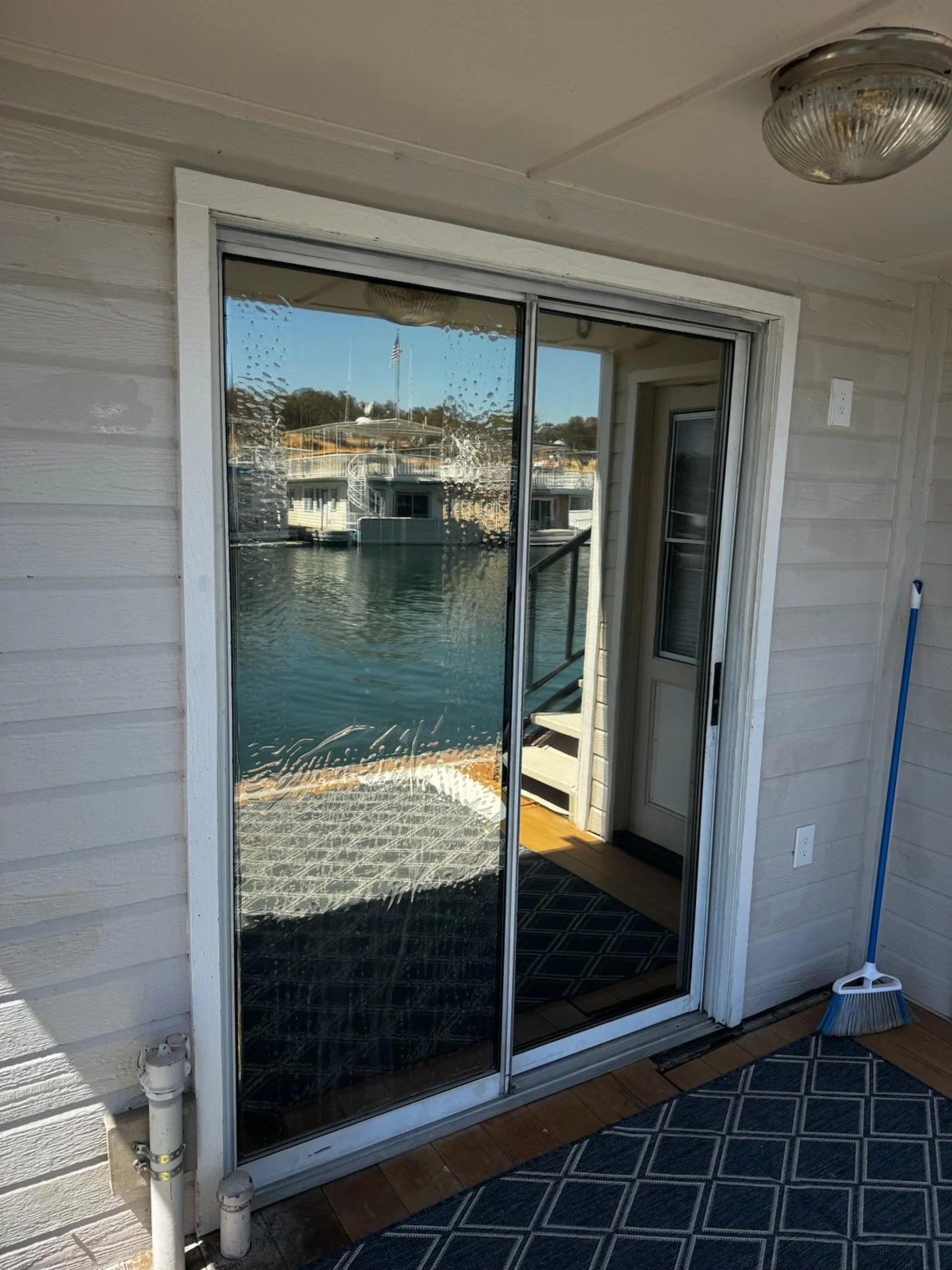 Sliding glass door on water-front porch, with raindrops on glass, outdoor scene of boats and a flag in distance, and indoor view of a door and stairs.