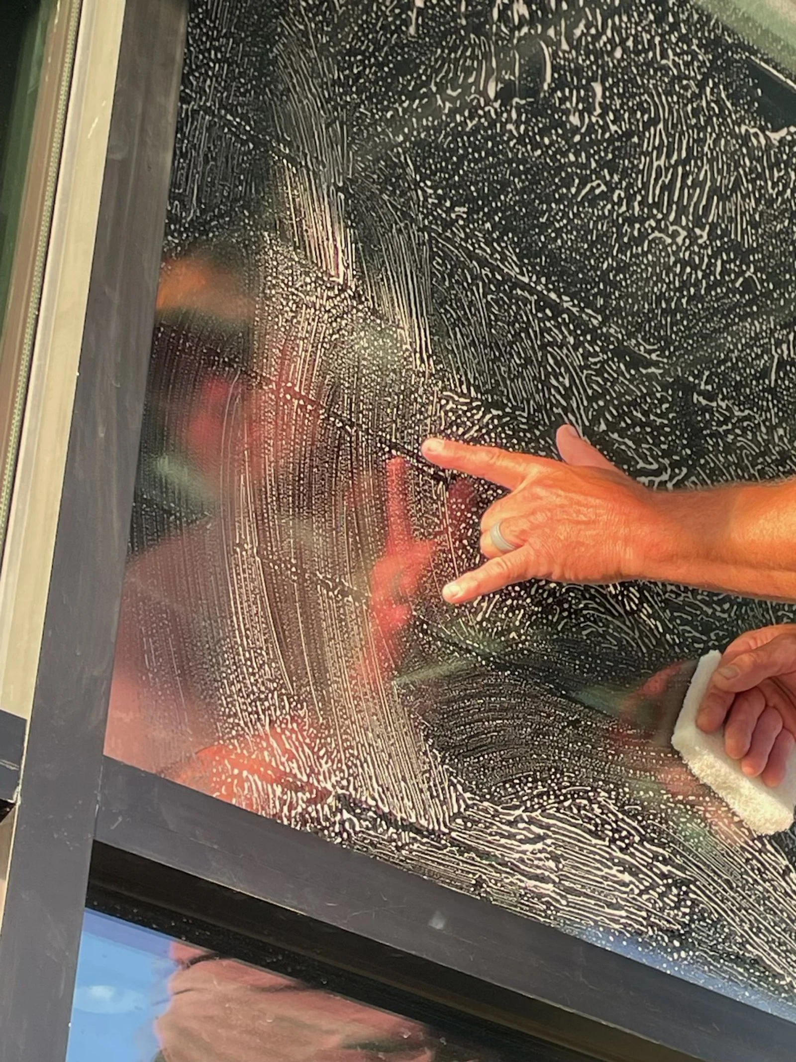 A person cleaning a glass window with a white cloth, leaving soap suds and streaks on the glass surface.