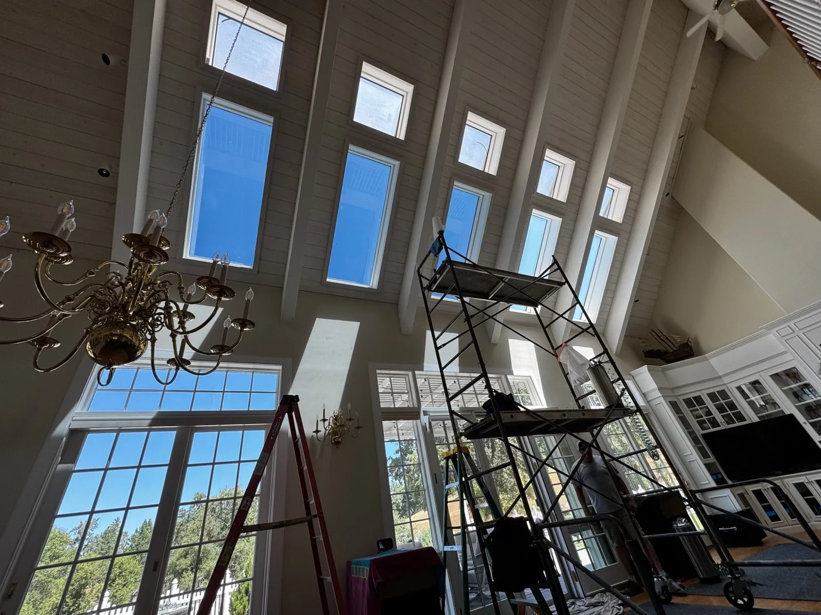 Interior view of a room with large windows, a chandelier, and scaffolding for construction or renovation work.