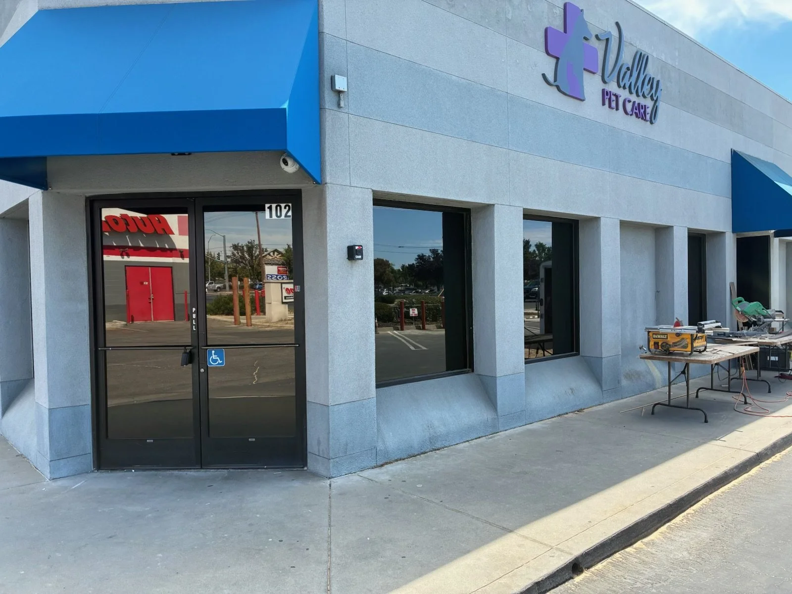 Exterior of Valley Pet Care building with blue awnings, glass doors, and scissors on a table outside.