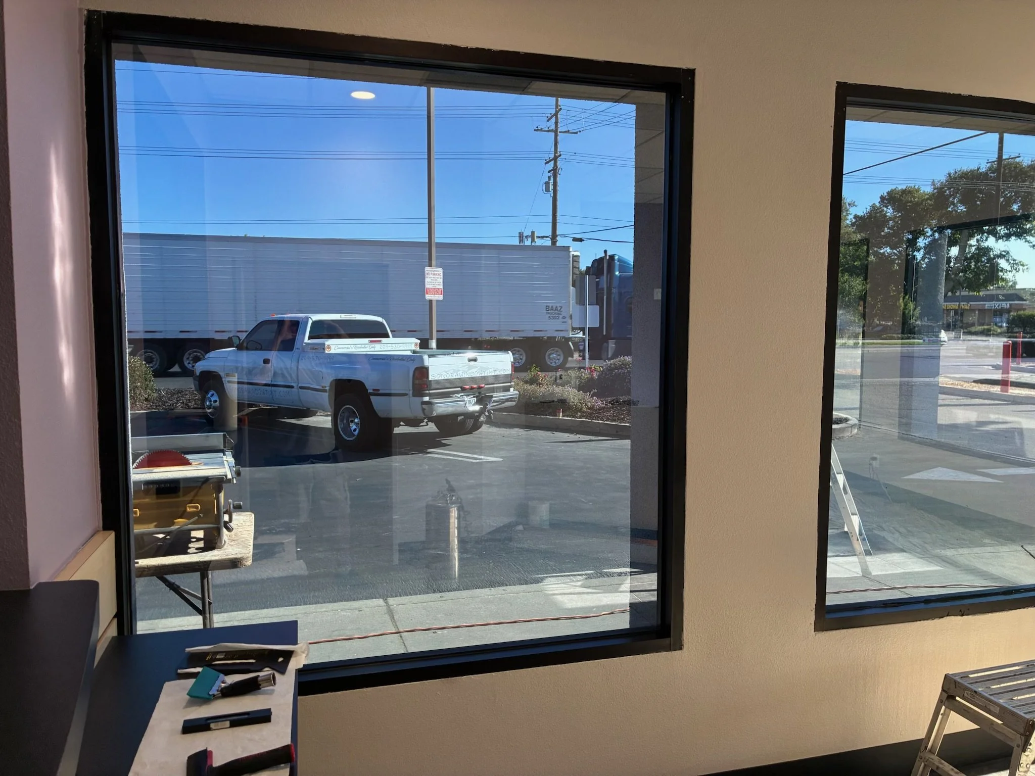 View through office window showing parking lot with a white pickup truck and a large semi-truck in the background.