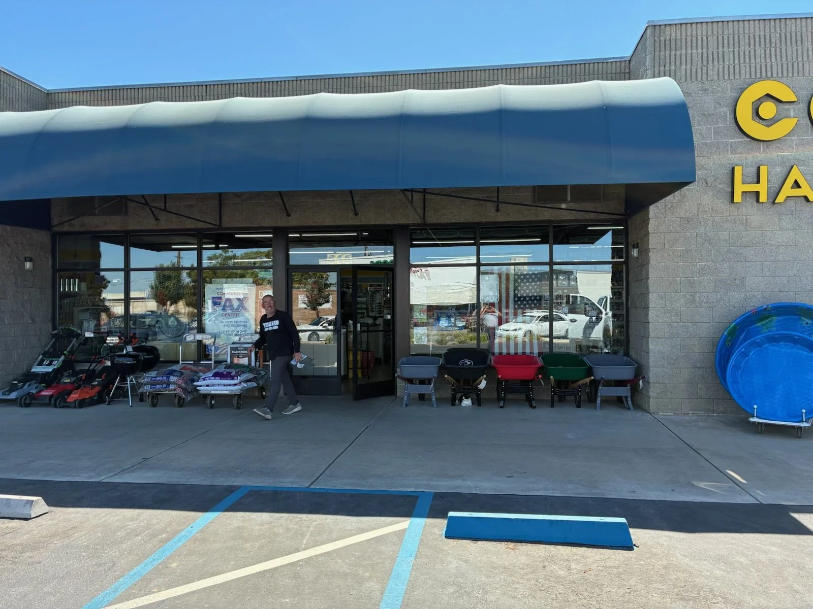Storefront with outdoor display of lawn equipment and gardening supplies, person walking outside.
