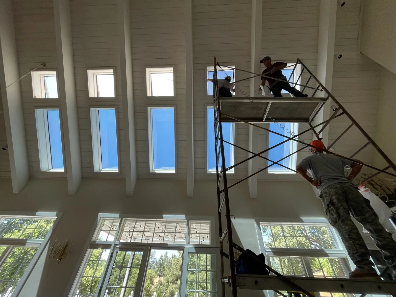 Construction workers on scaffolding inside a building with large windows and a high ceiling.