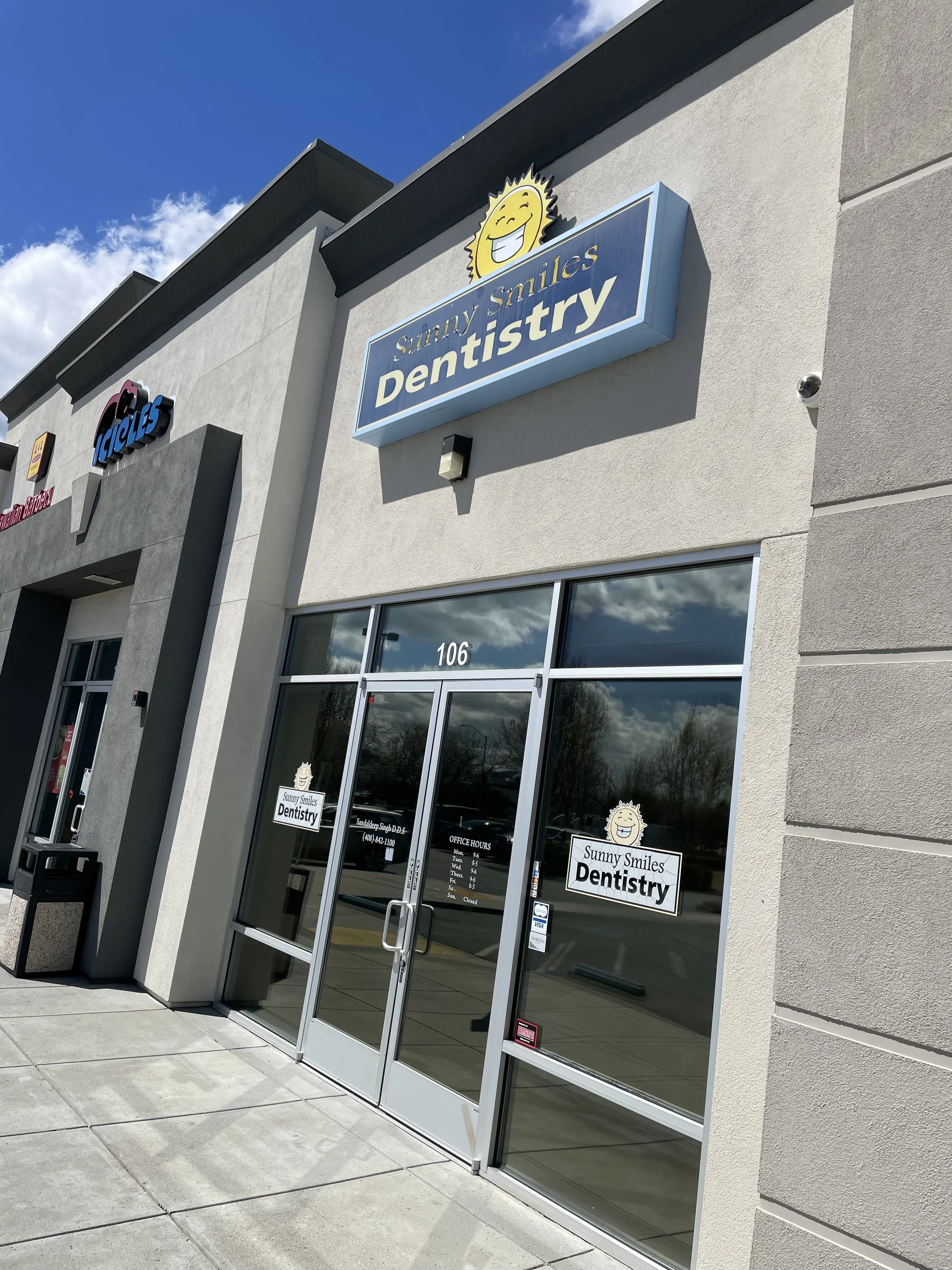 Exterior view of Sunny Smiles Dentistry office with glass doors, signage, and a clear sky with some clouds.