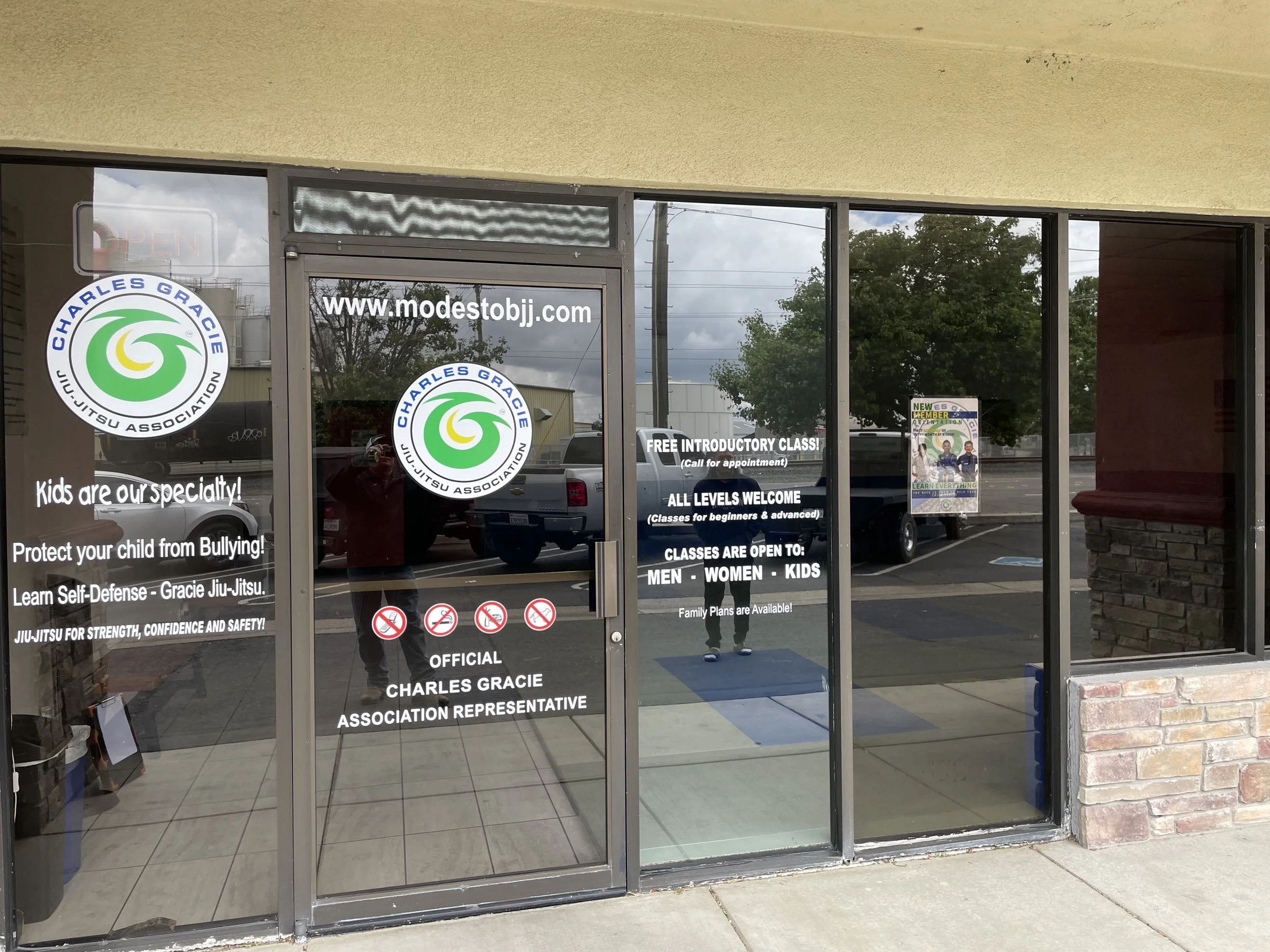 Martial arts dojo storefront window with logos, website, and text about classes, policies, and safety.