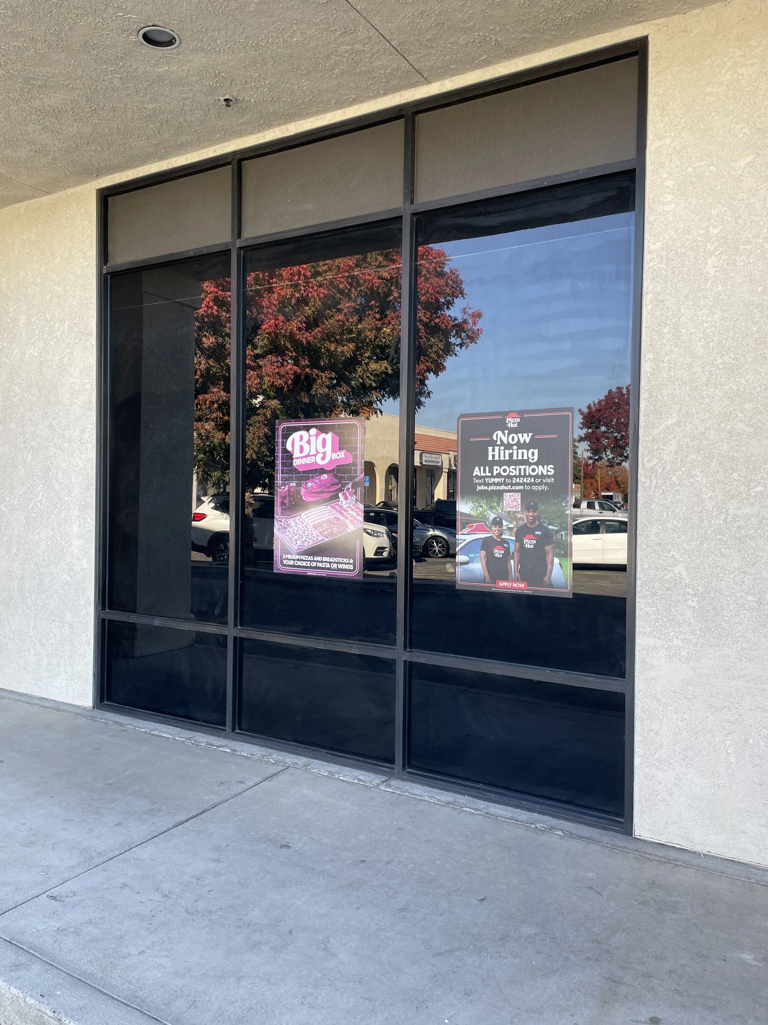 Two posters taped to the glass window of a building. One advertises a Big Dinner Box and the other indicates that the business is now hiring for all positions.