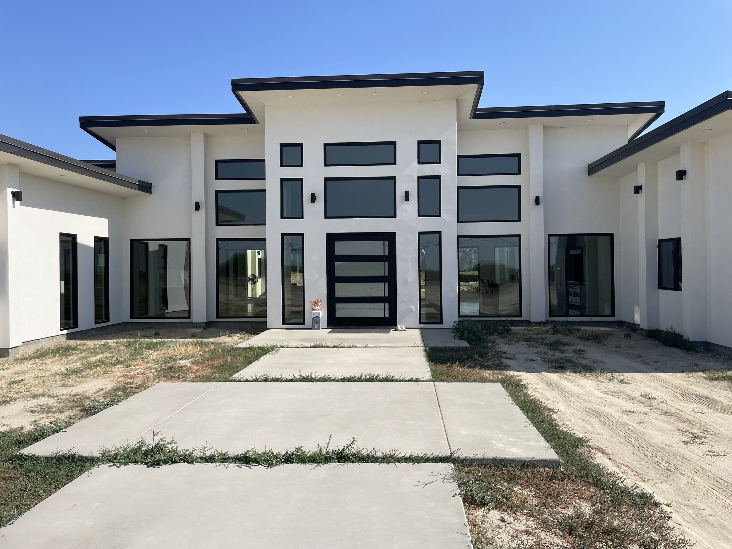 New modern house with a black front door, large windows, and white exterior walls, under a clear blue sky.