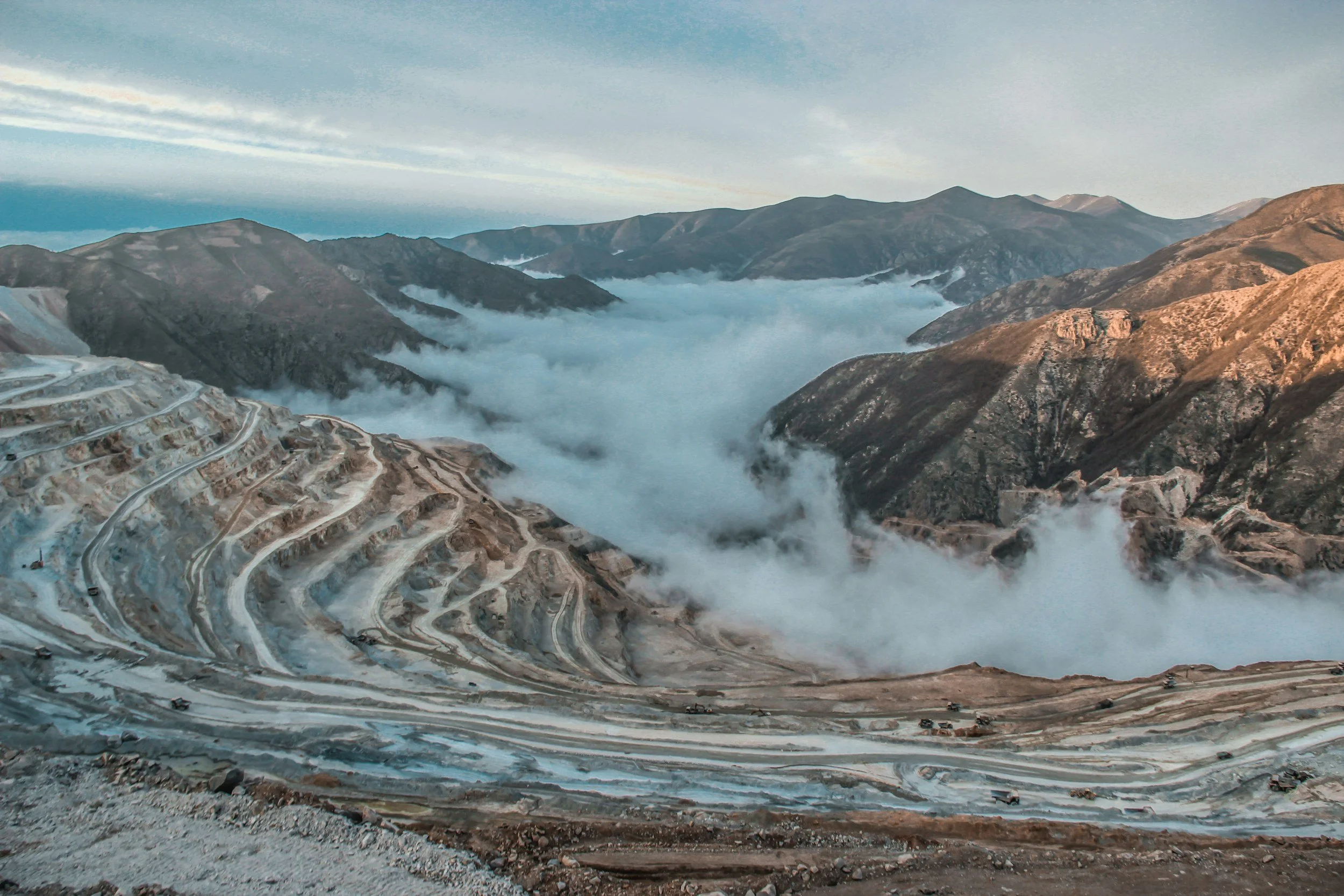 Terraced mountainside with winding dirt roads and a fog-filled valley in a remote landscape.