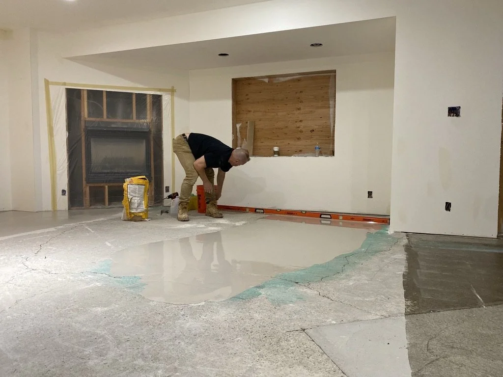 An eco floors employee working on leveling a concrete floor inside a room under renovation, with some primer and wet self leveler over it.