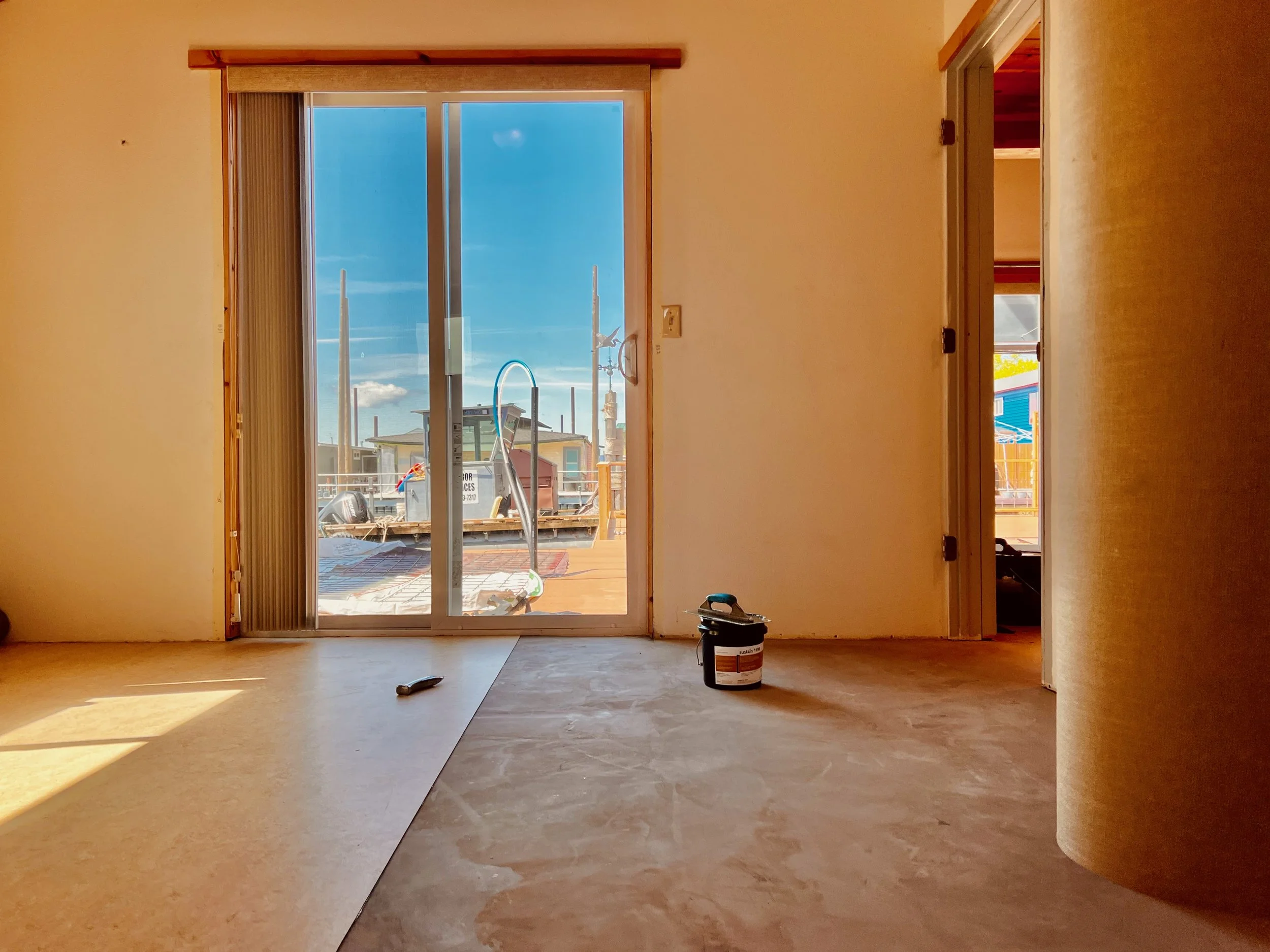 Interior room with a prepared subfloor, marmoleum sheet being installed, a knife, and forbo sustain 1195 adhesive.