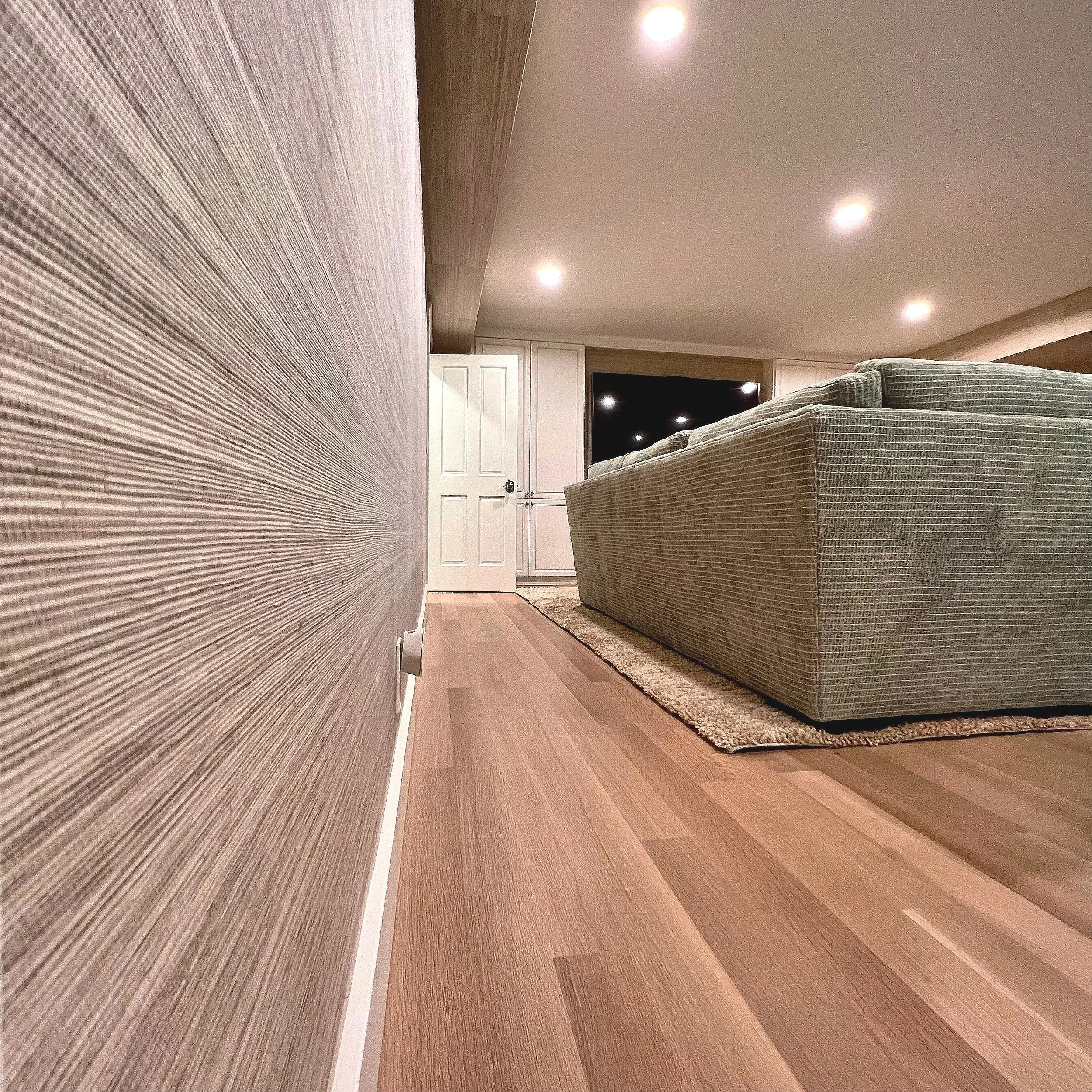 Living room with beige striped carpet, beige and brown upholstered furniture, white closet doors, and dark TV mounted on the wall