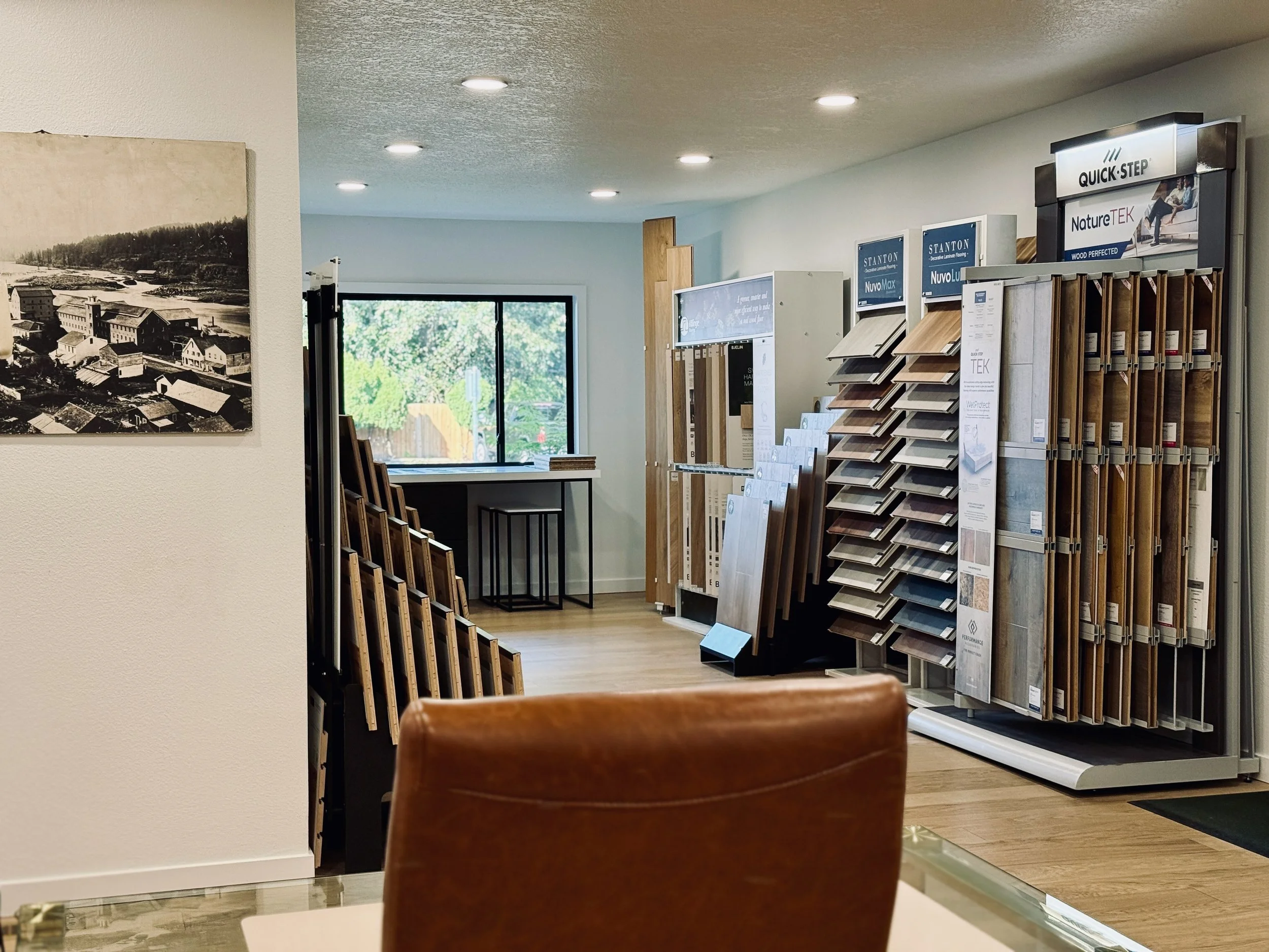 Interior of Eco Floors Portland Showroom display racks of hardwood and laminate flooring options, with a window in the background and a large black-and-white landscape photo on the wall.