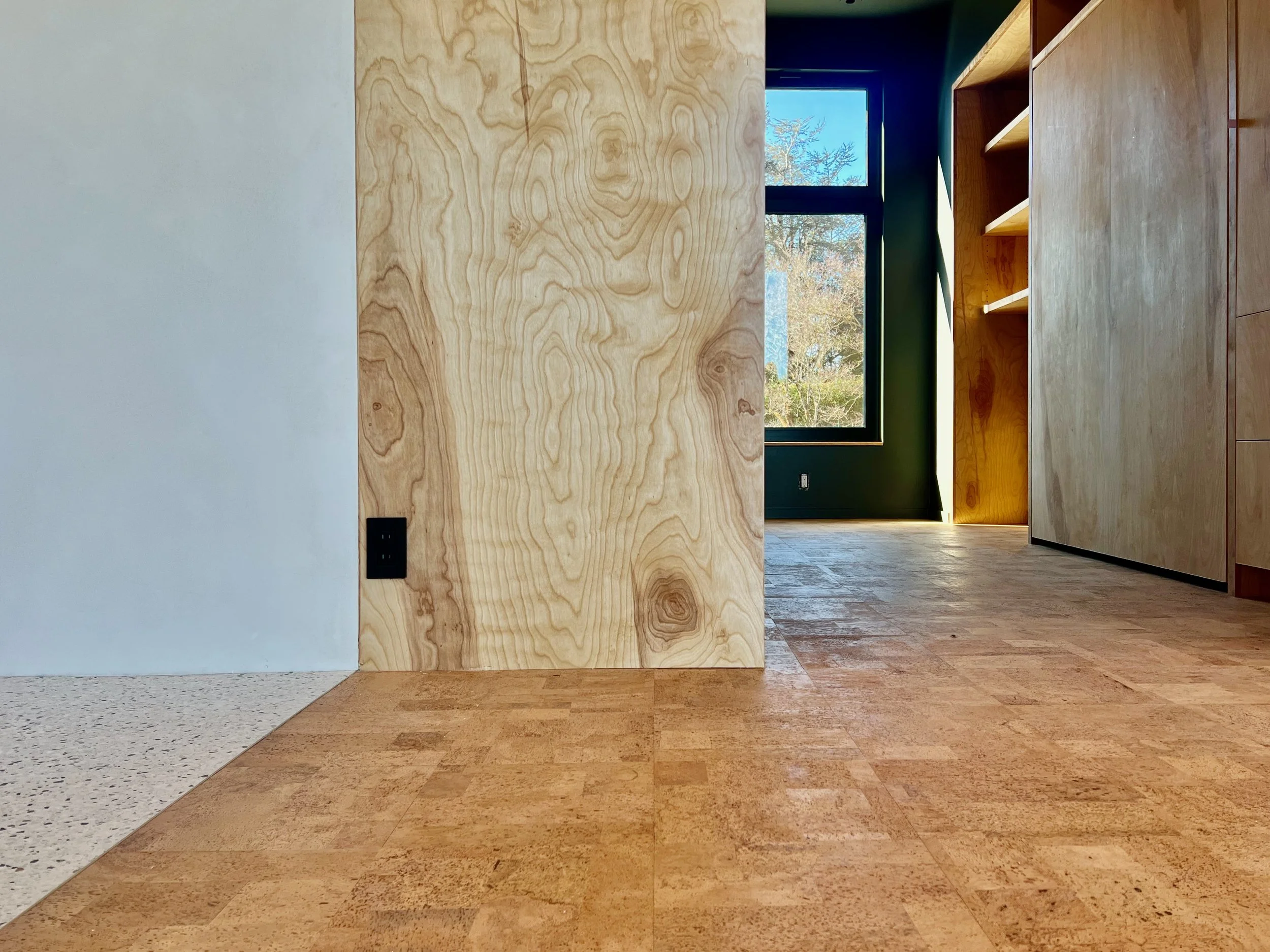 Interior of a room with a natural wood wall, a window showing trees outside, and a mix of wood and tile flooring.