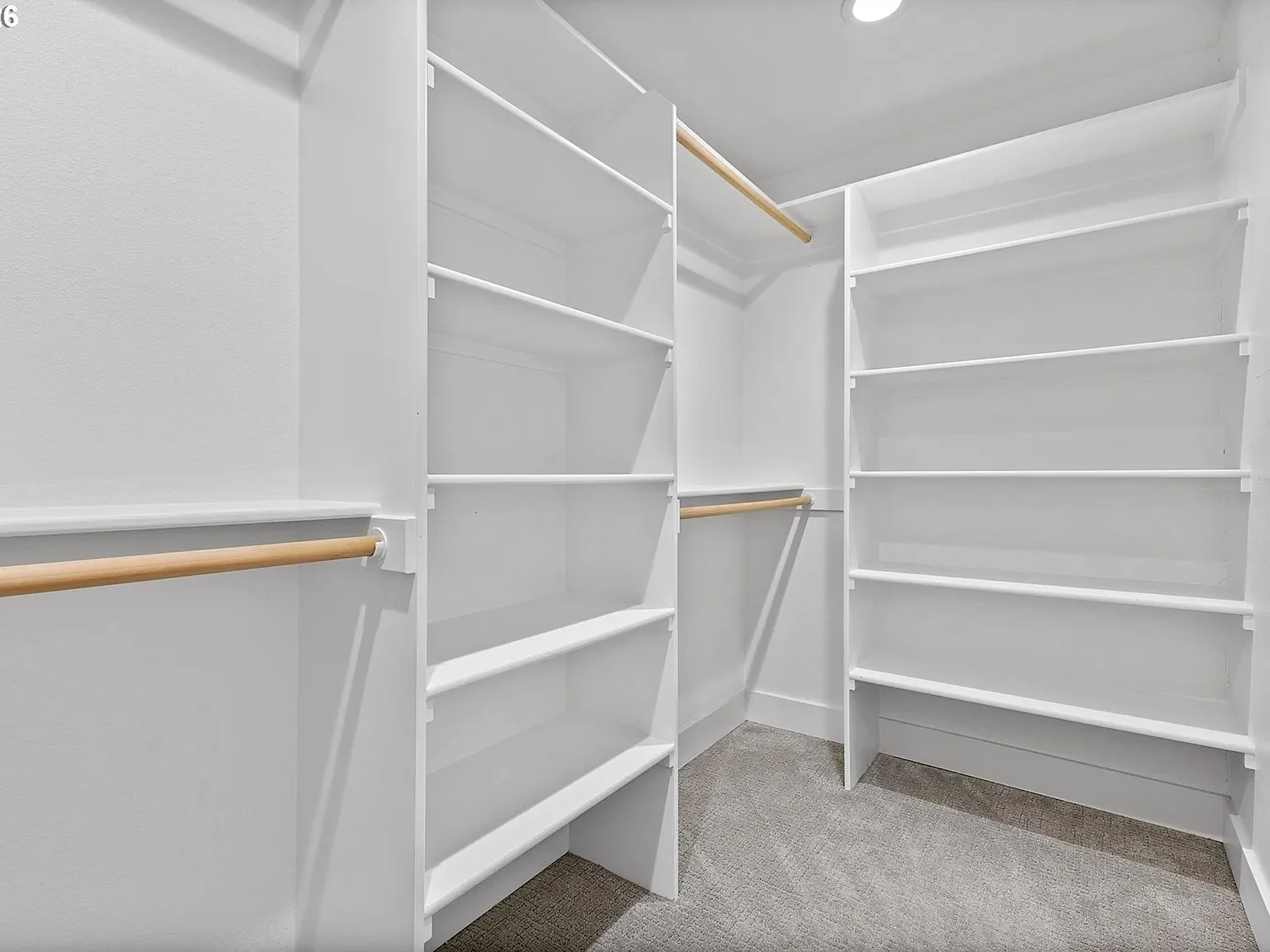 A walk in closet white grey carpet and bright white shelving.