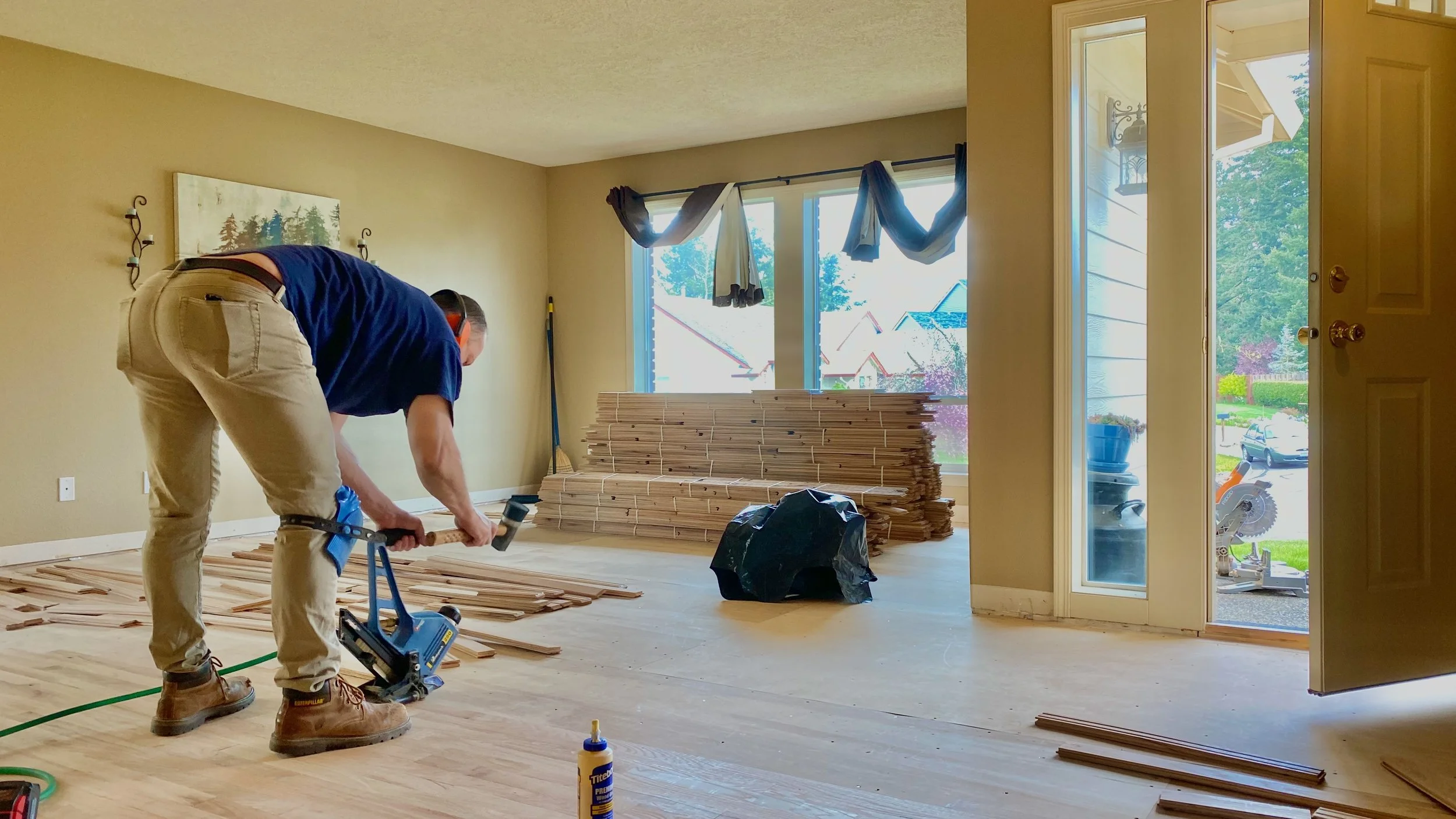 An eco floors employee installing hardwood flooring in a living room with large windows