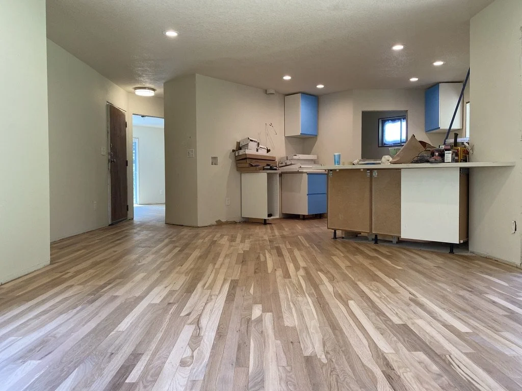 Empty kitchen with wooden floors, partially installed cabinets, and a small window.