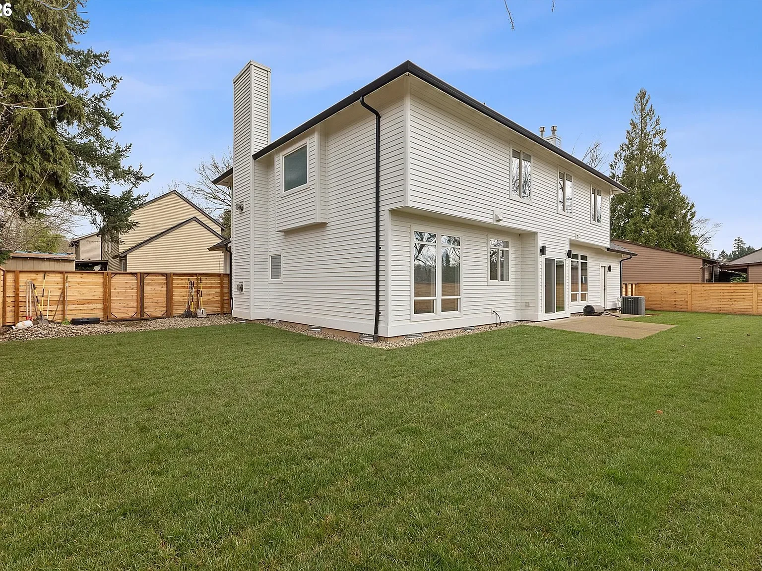 Back yard of a white home with green grass and a modern wood fence.
