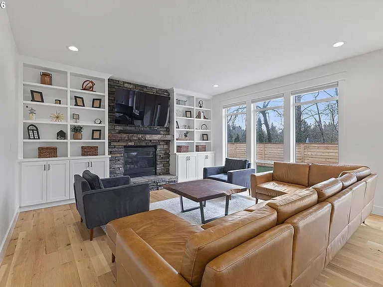 Bright living room with hardwood floors, stone fireplace, and white shelving.