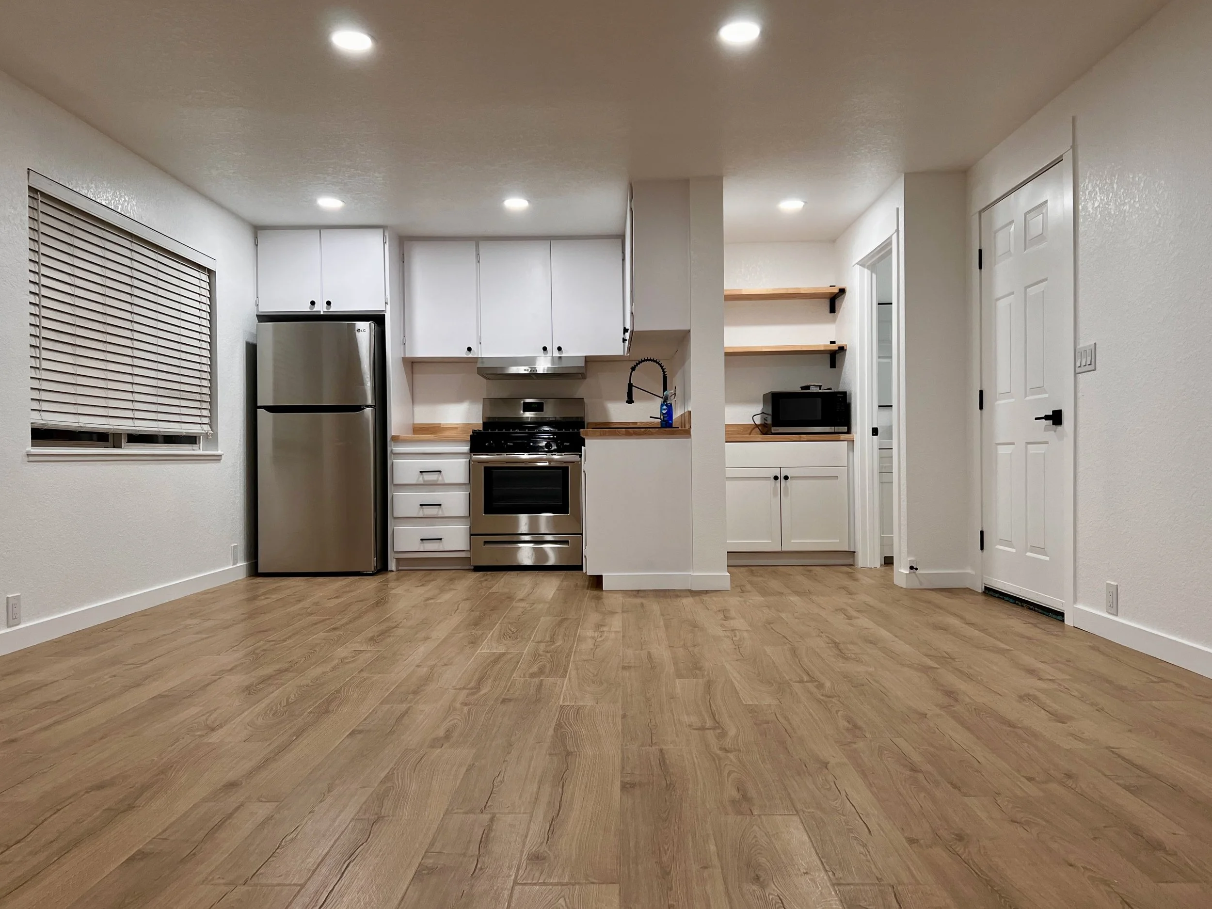 Remodeled kitchen with white cabinets, butcher block counters, stainless steel appliances, and light oak laminate flooring. 