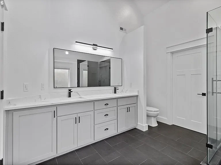 Spacious master bathroom with black Italian tile, light grey vanity, a large black mirror, bright light bar, and black fixtures. 