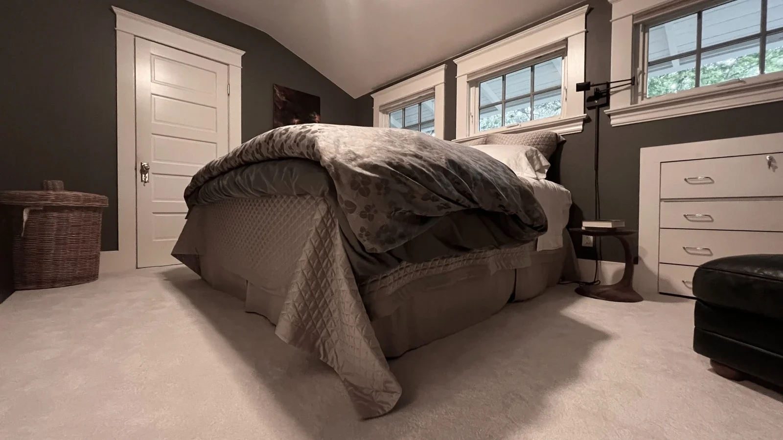 Portland home bedroom in the Hawthorne neighborhood with white plush carpet, white wood trim work, a bed with a thick comforter, and a wooden nightstand.