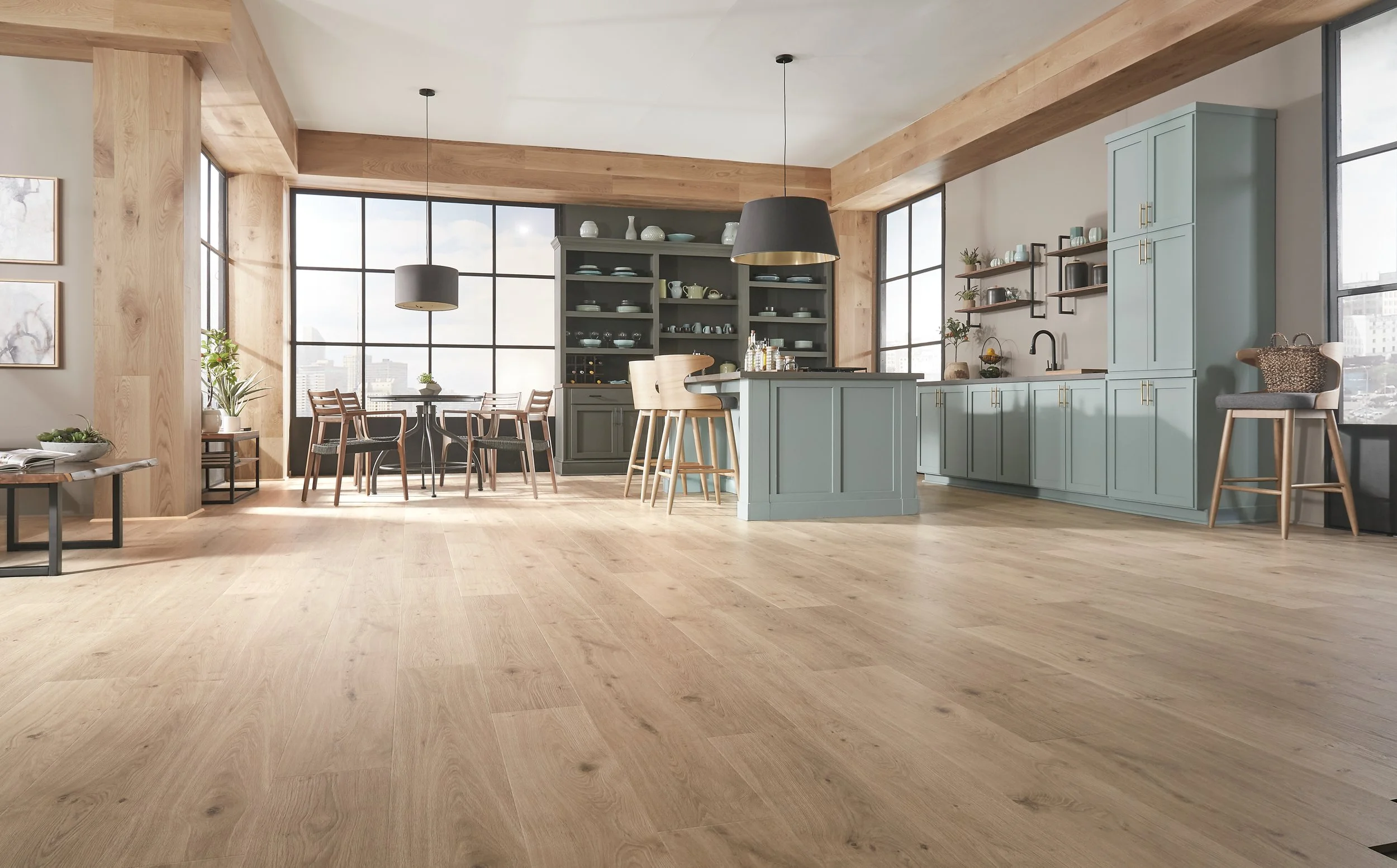 Modern open-concept kitchen and dining area with large windows, light wood flooring, and a mix of green and grey cabinetry. Includes a kitchen island, dining table with chairs, and decorative vases and plants.