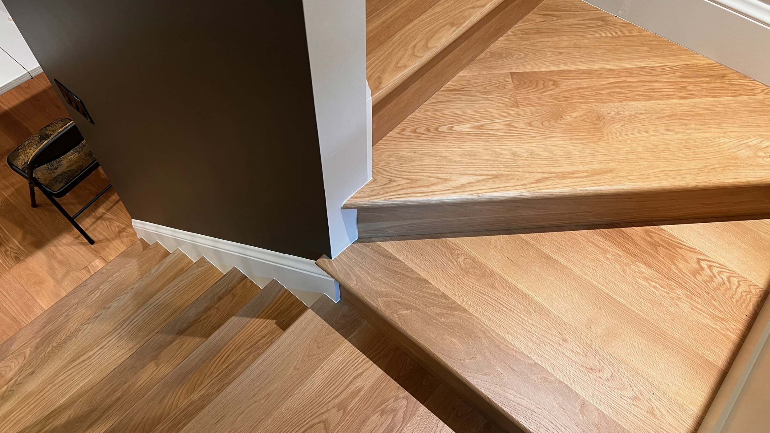 Wooden staircase with a dark wall and a patterned chair at the bottom.