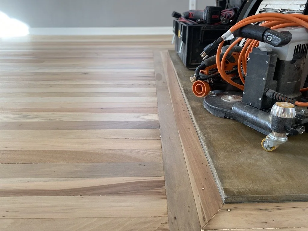 Close-up of a wooden floor, showing a section with a step-up or platform, with construction tools and equipment on the platform.