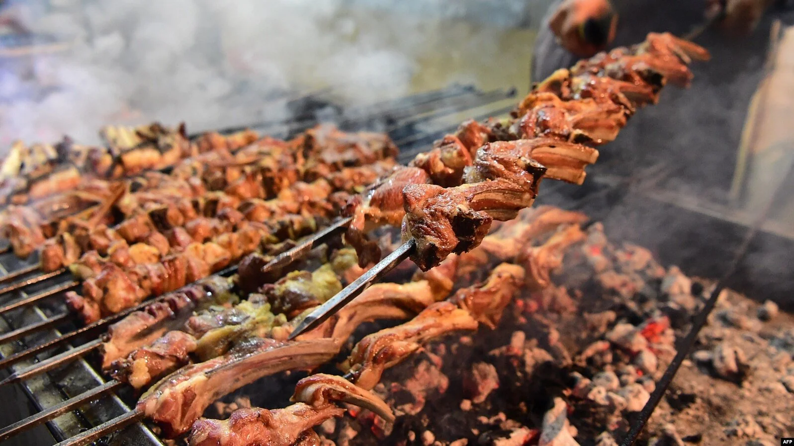 Skewers of grilled meat being cooked over open flames with glowing coals underneath.