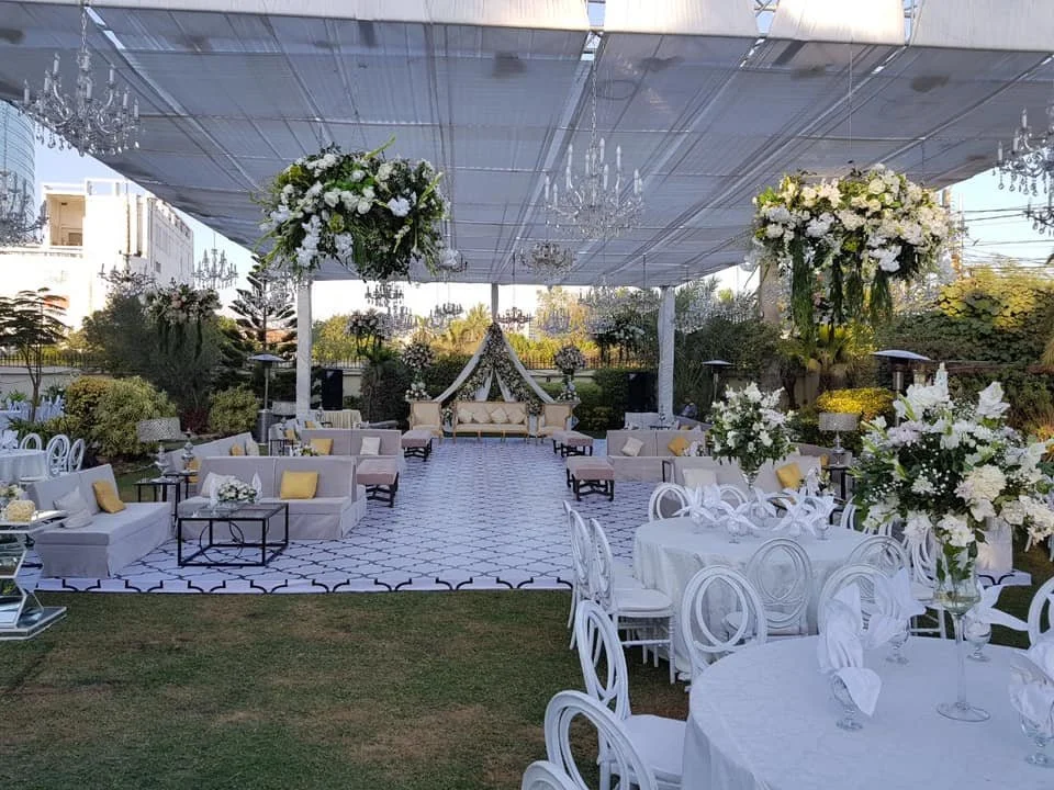 Elegant outdoor wedding reception setup with floral arrangements, chandeliers, and a decorated stage area under a canopy.