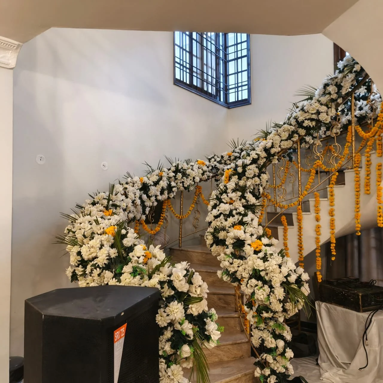 Decorated staircase with white and yellow flowers, garlands, and gold accents in an indoor setting near a window.