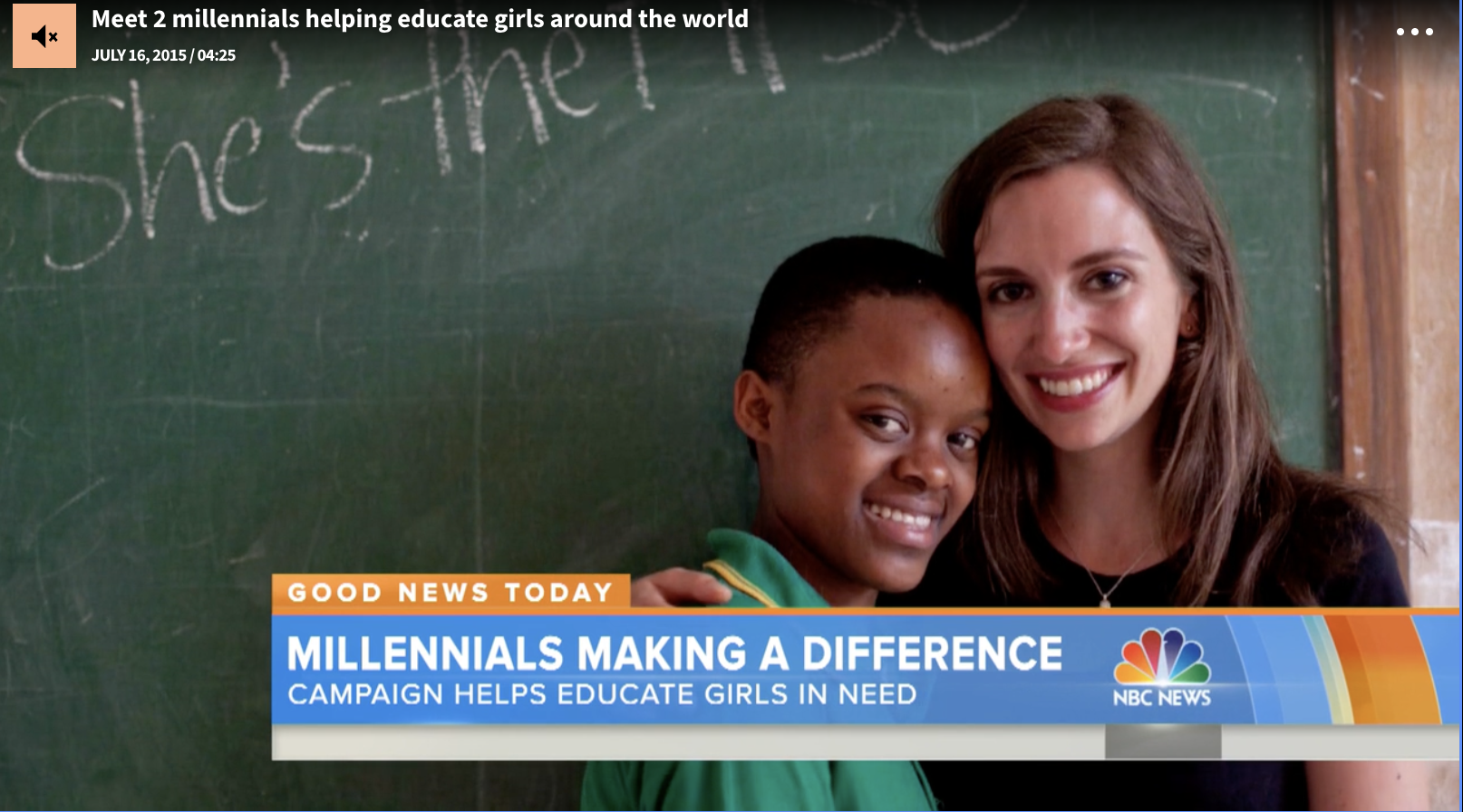 Two millennials, a girl of African descent and a woman of Caucasian descent, smiling and hugging each other in front of a chalkboard with writing in a classroom.