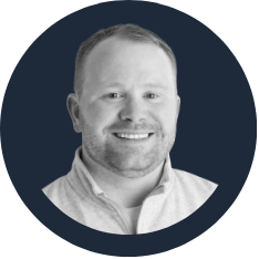 Black and white photo of a smiling man with short hair and a beard, wearing a collared shirt.