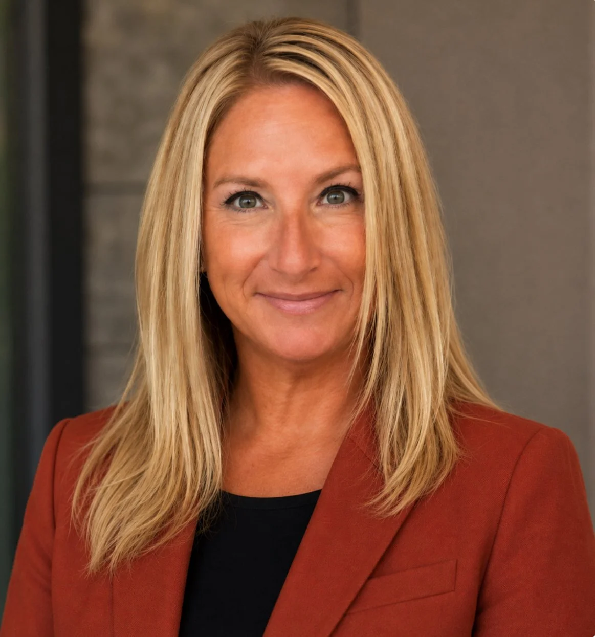 Portrait of a woman with blonde hair smiling against a dark background.
