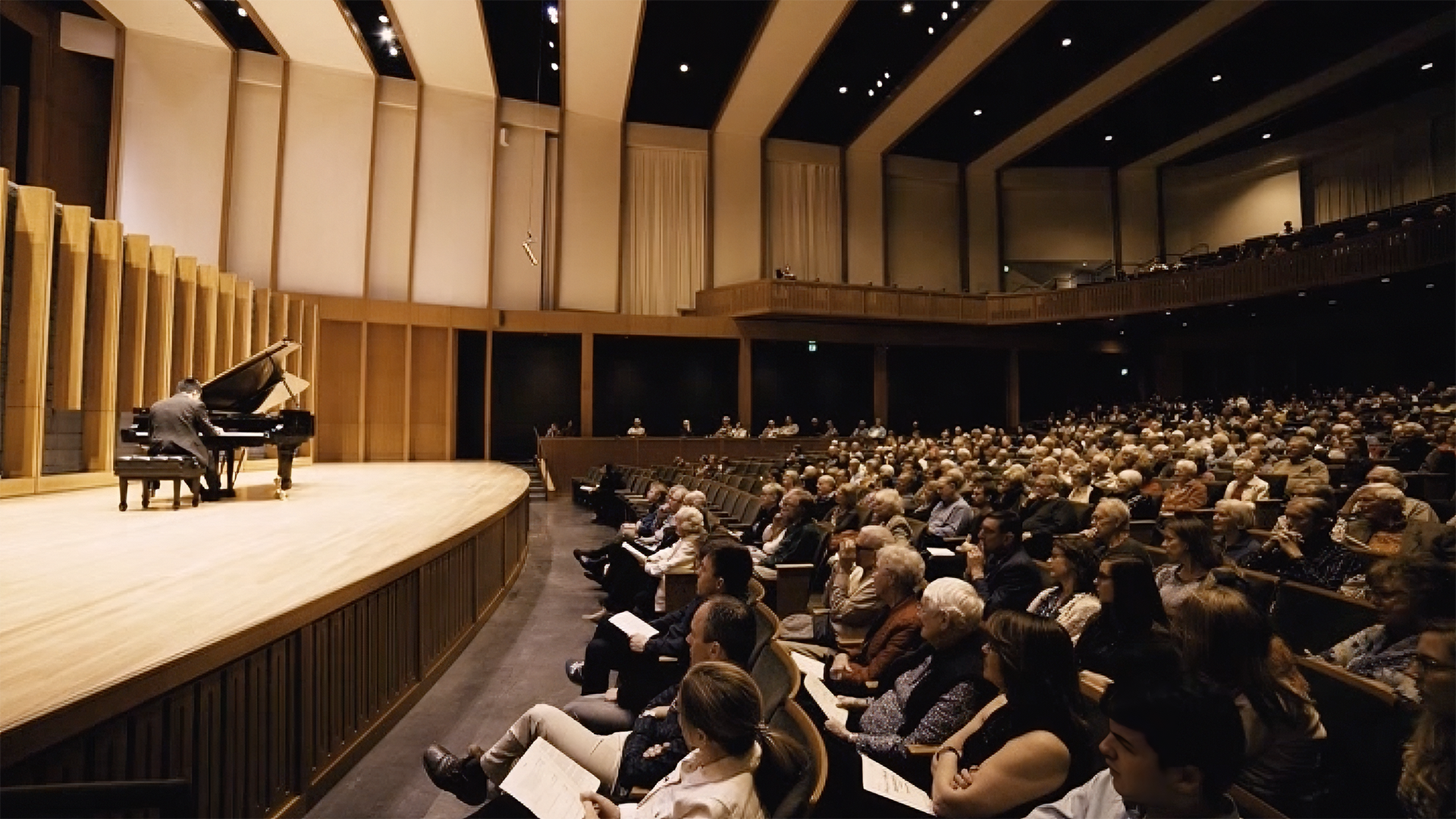 An auditorium filled with seated audience members watching a pianist perform on stage.