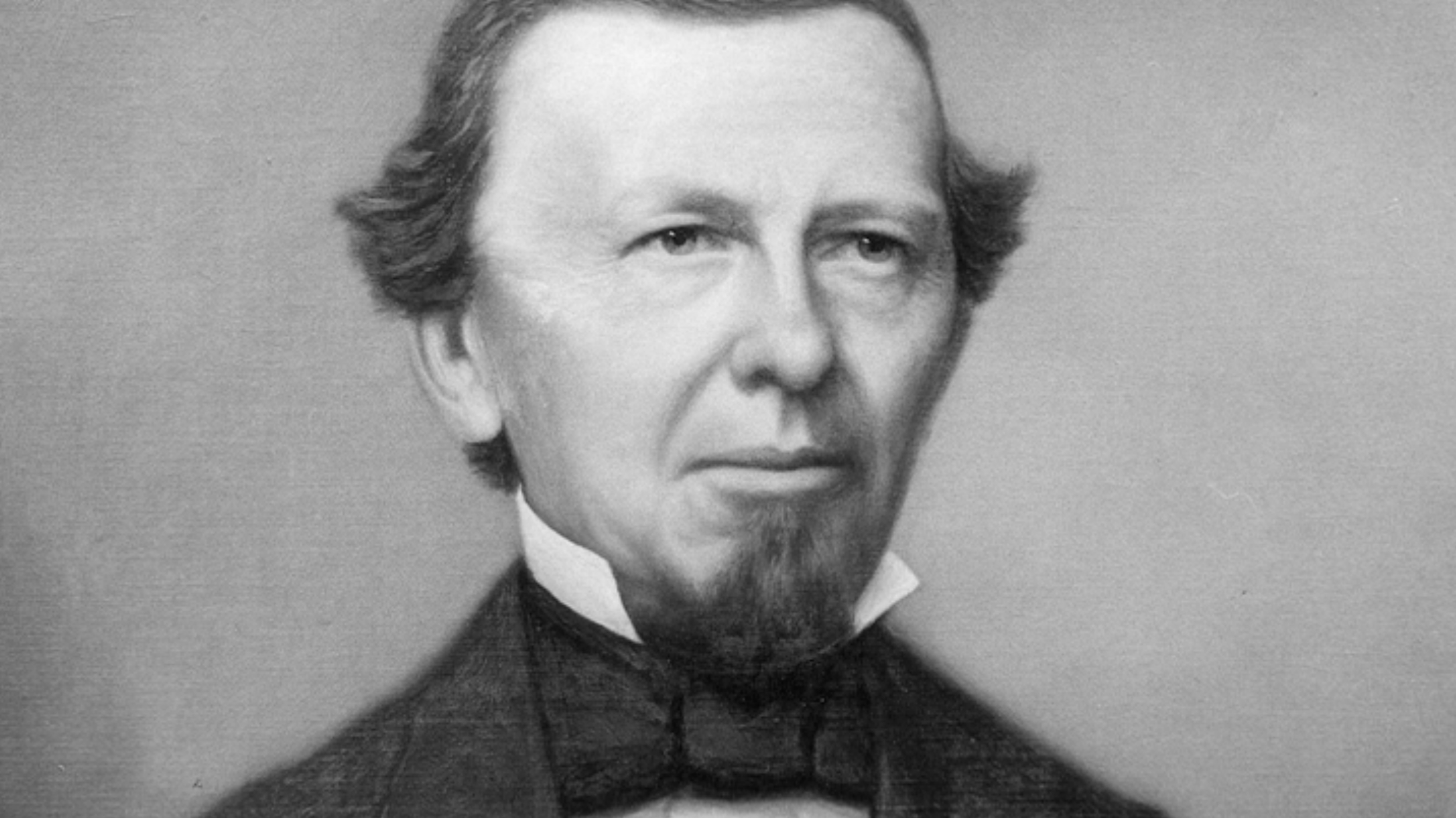 Black and white portrait of a man with a beard, wearing a suit and bow tie from the 19th century.