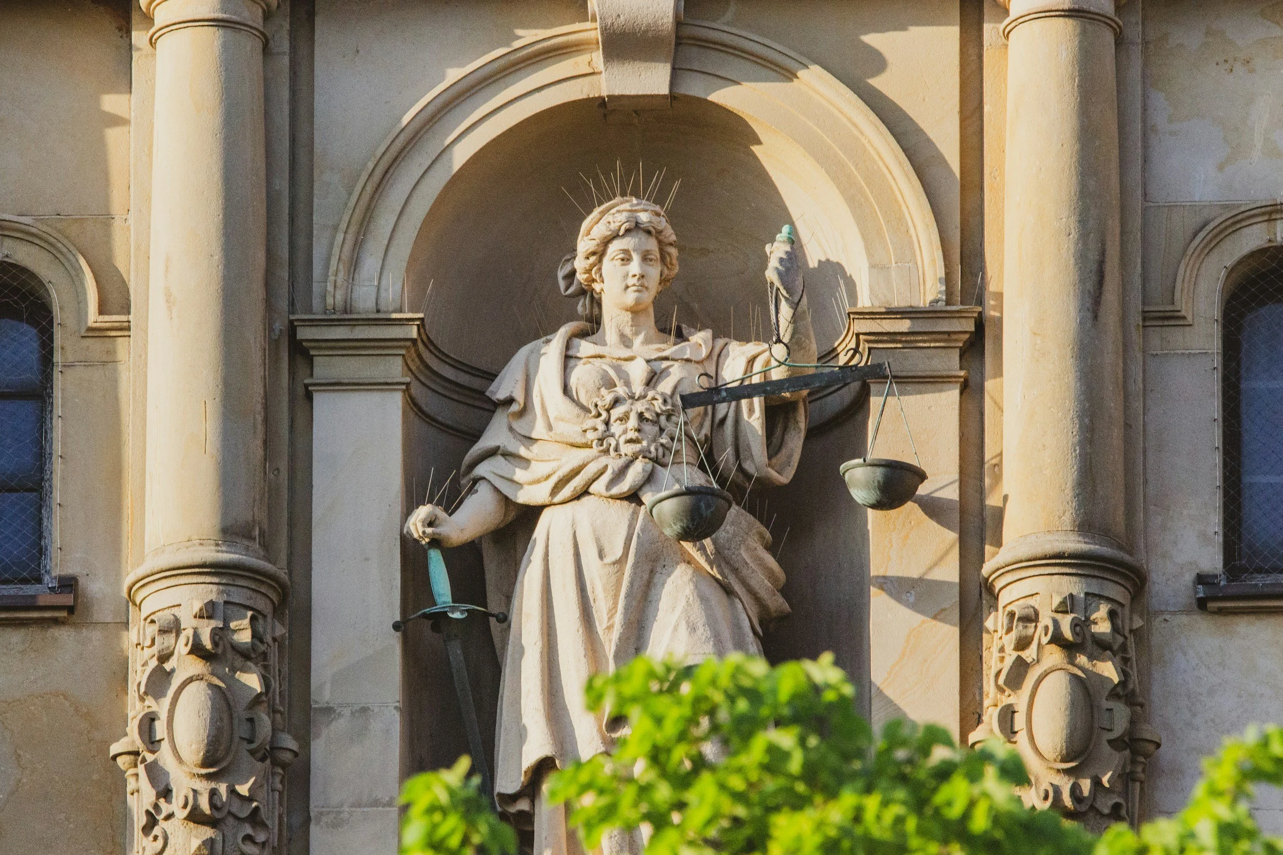 Statue of Lady Justice with a blindfold, holding a sword and scales, mounted on a building facade.