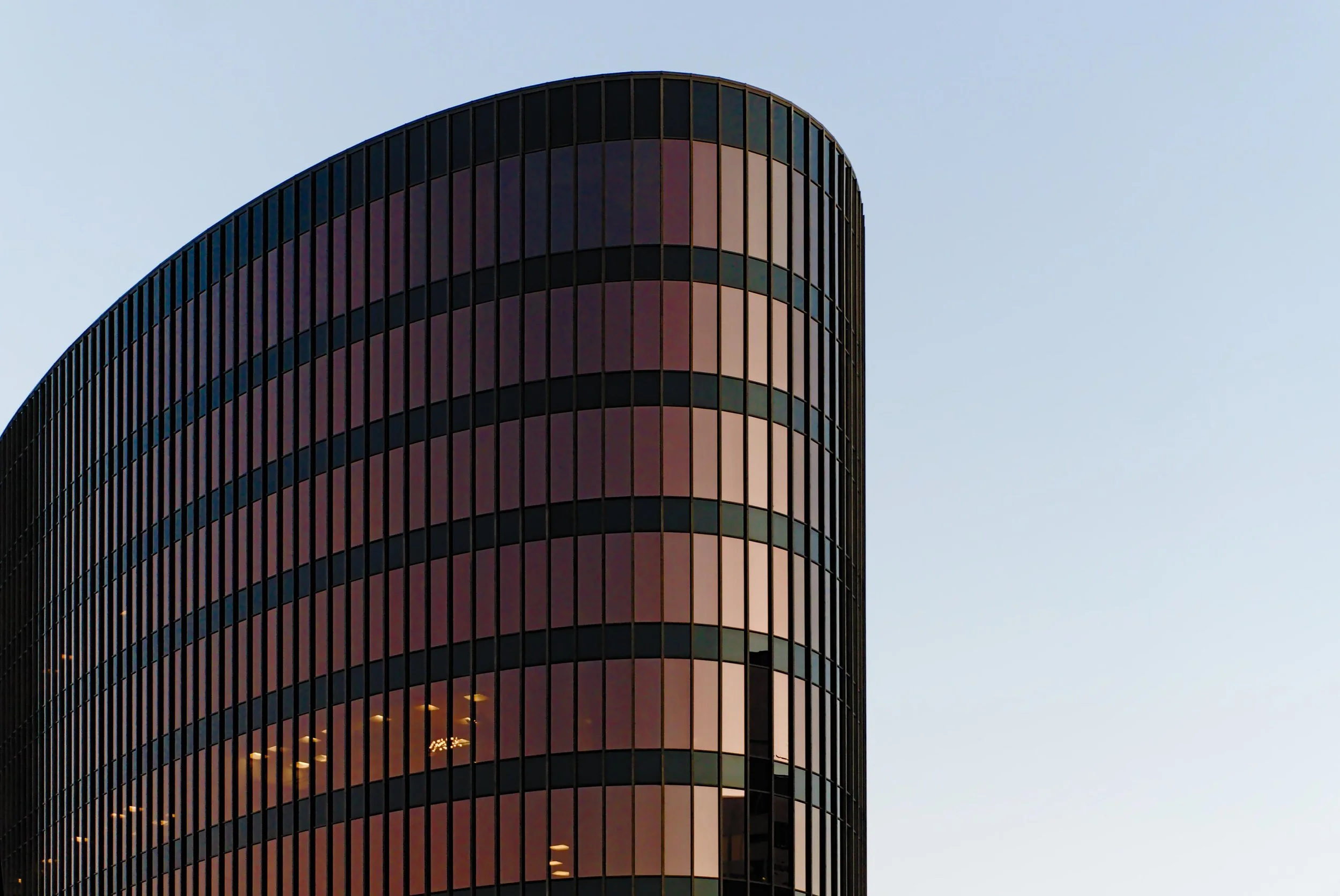 A tall modern office building with curved glass exterior reflecting the sky, against a clear blue sky.