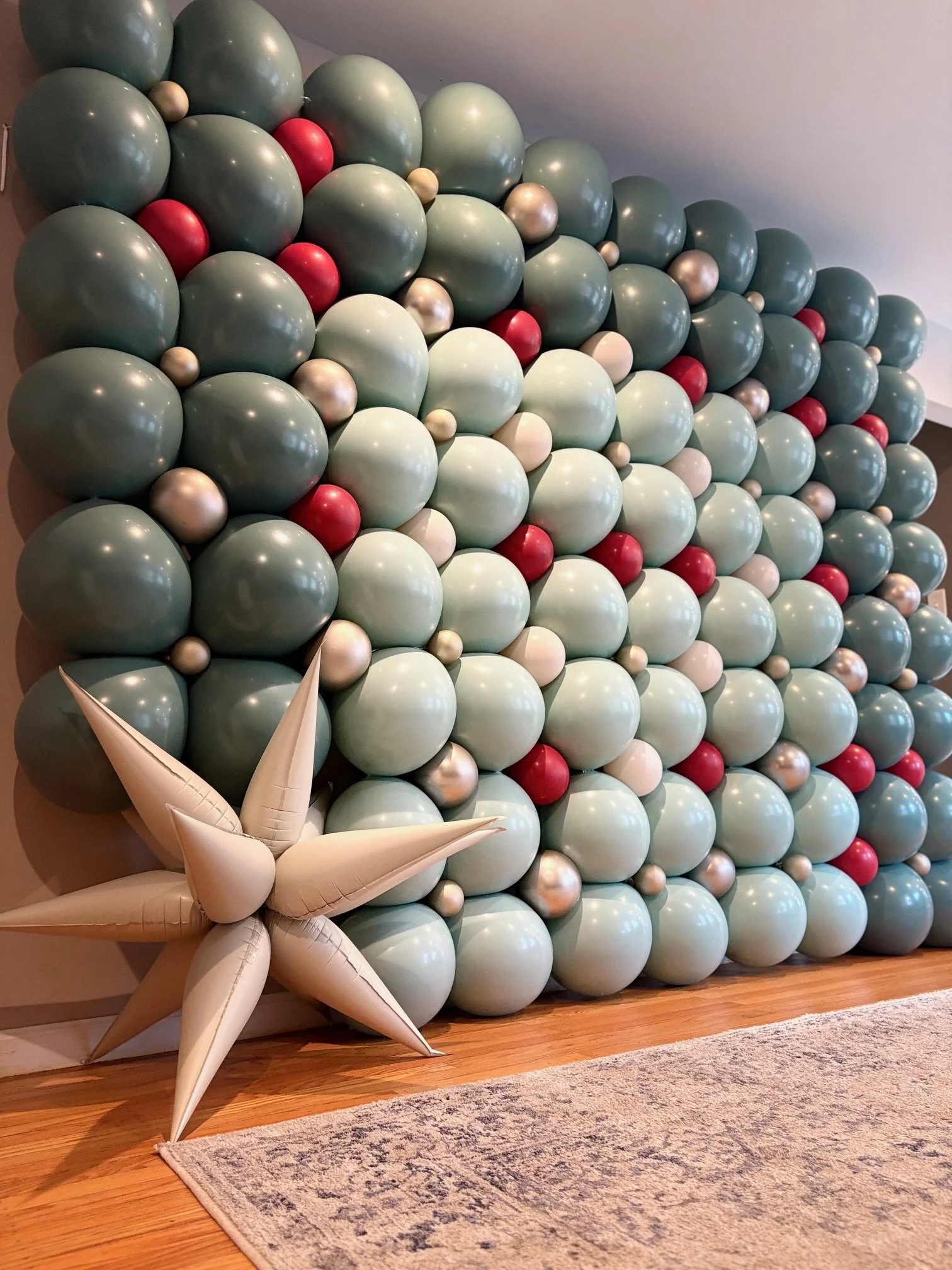 Decorative wall adorned with green, red, white, and silver balloons arranged in a pattern, with a large cream-colored balloon star decoration at the bottom left corner.